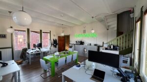 Modern kantoorinterieur aan het Damrak met witte bureaus, een felgroene vergadertafel en een neonlicht met de tekst "ENDYMION" aan de muur.