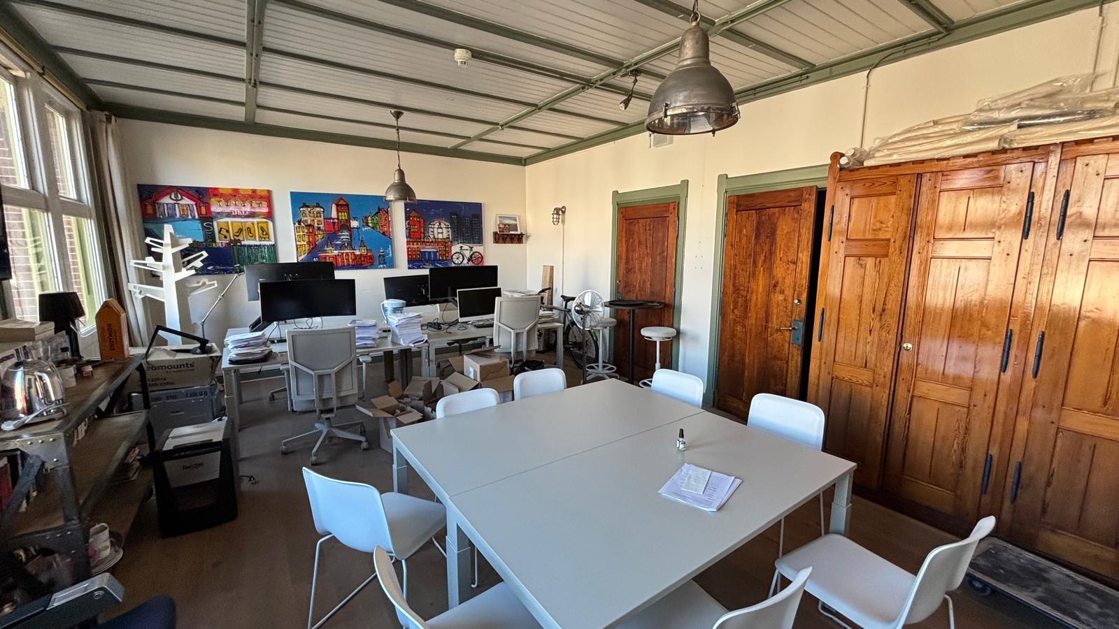 Moderne kantoorruimte aan het Damrak met witte bureaus, houten kasten en kleurrijke kunst aan de muur.