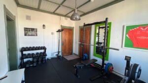 Kleine fitnessruimte met krachttrainingsapparatuur, gewichten en een roeimachine bij Damrak 246 in Amsterdam.
