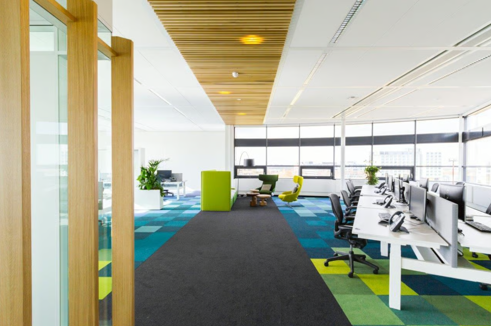 Modern open-plan office space on Boeing Avenue with colorful carpet tiles, shared desks, and lounge seating areas.