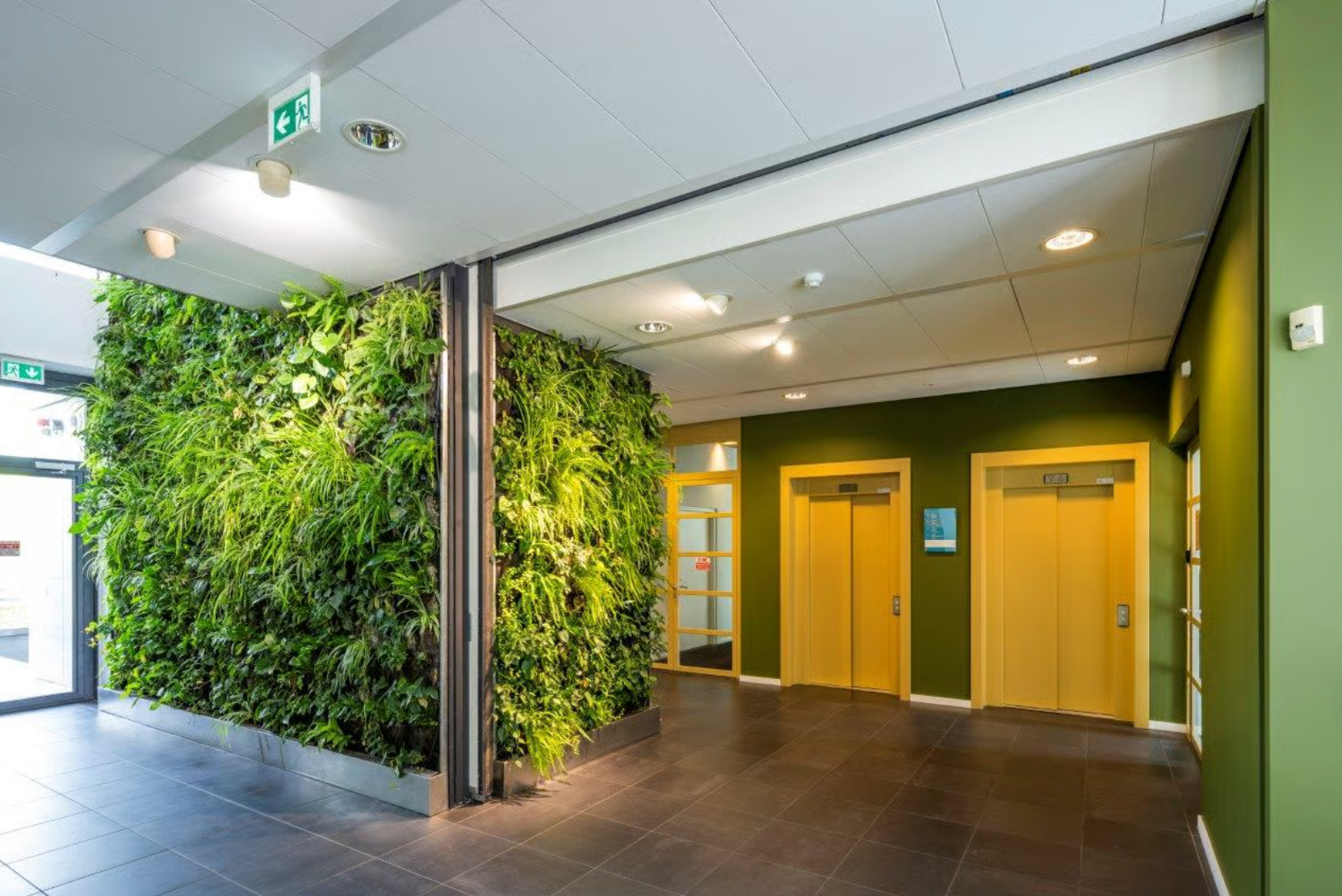 Modern office lobby with a green plant wall and two yellow elevators on Boeing Avenue.