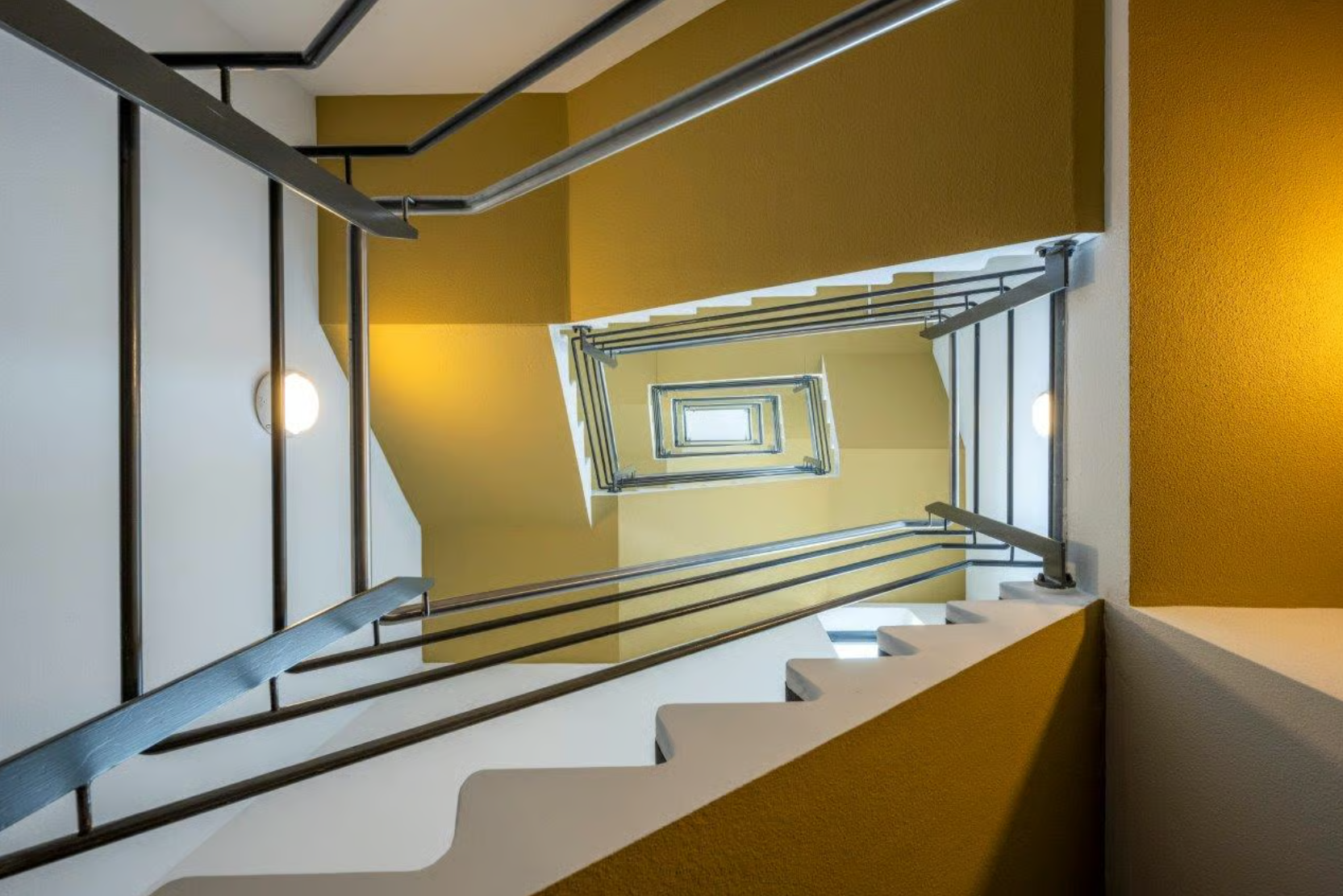 View looking up a modern spiral staircase with yellow and white walls and metal railings on Boeing Avenue.