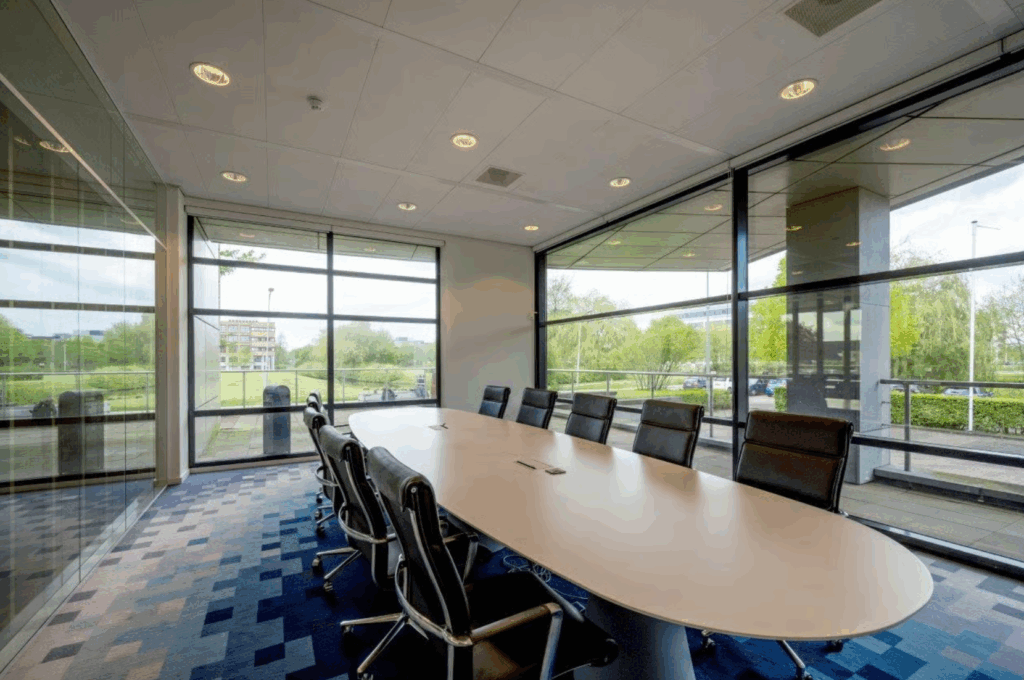 Modern conference room with a large oval table, black chairs, and floor-to-ceiling windows overlooking a green outdoor area on Boeing Avenue.