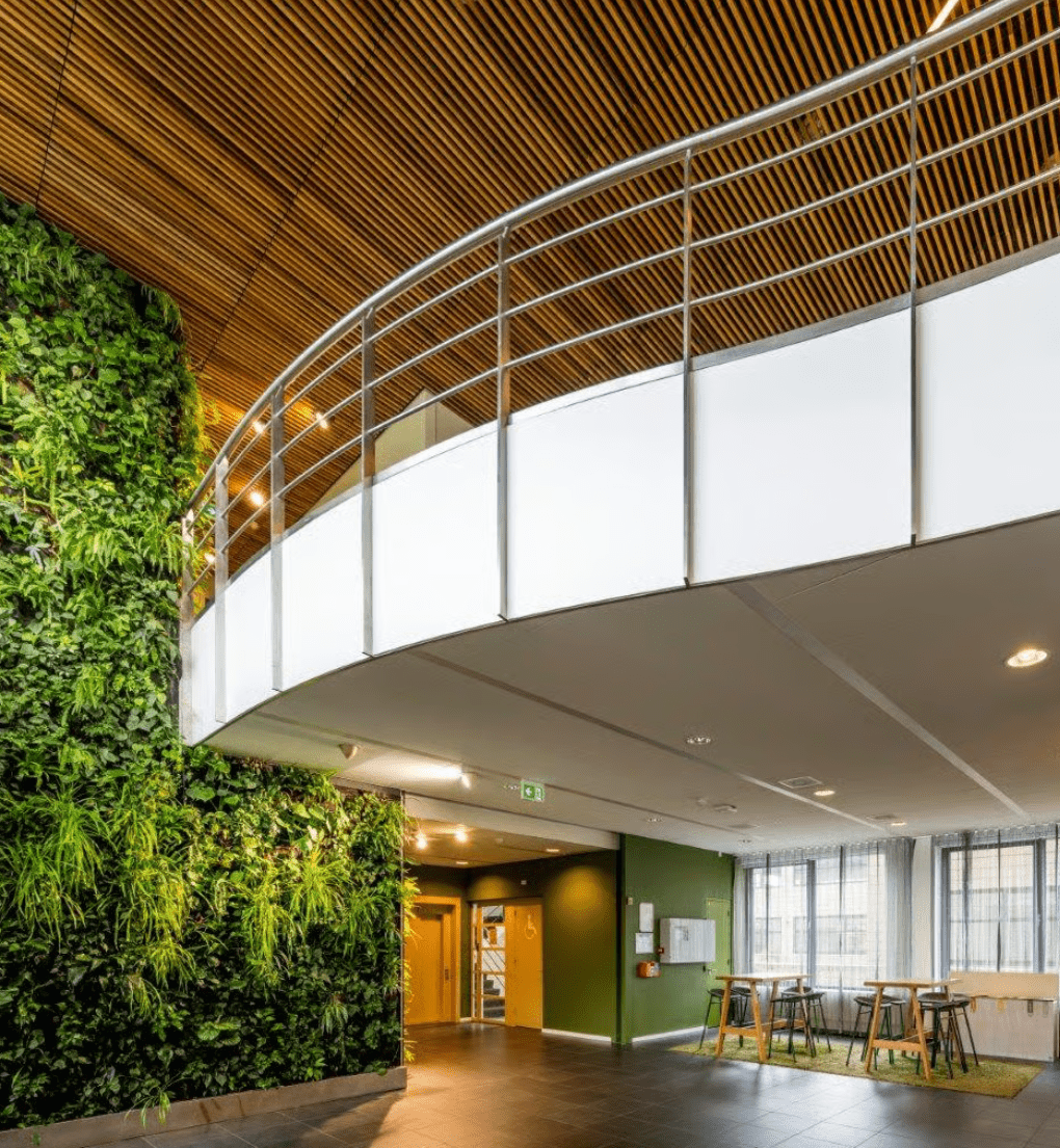 Modern office interior featuring a green living wall, wooden ceiling slats, and a curved upper-level walkway.