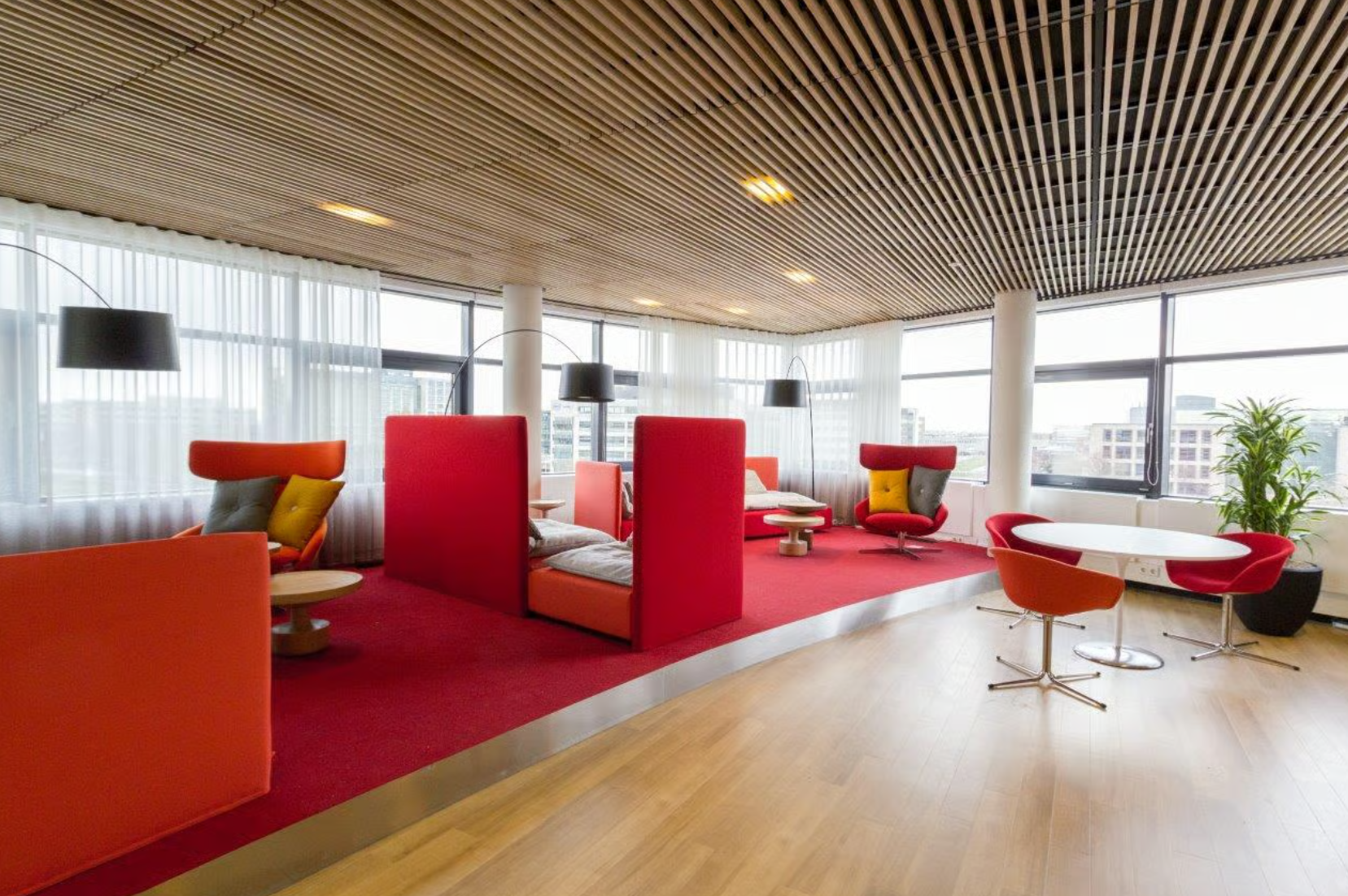 Modern lounge area at Boeing Avenue featuring red seating, round tables, and large windows with city views.