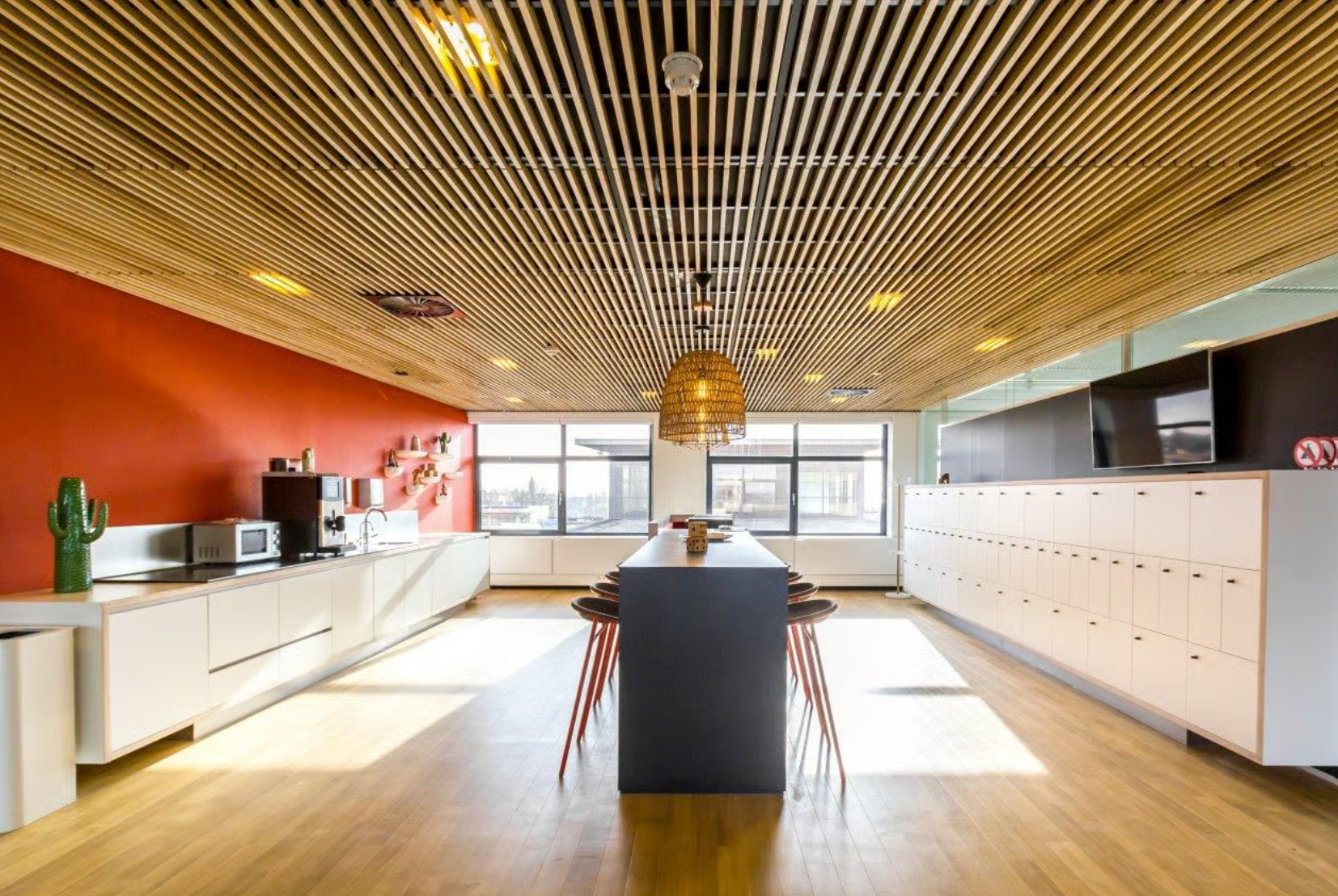 Modern office kitchen with a long central table, white cabinets, and a red accent wall on Boeing Avenue.