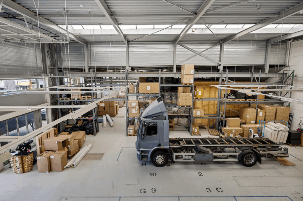 Interior view of a warehouse on Schaafstraat with shelves full of boxes and a partially assembled truck parked inside.