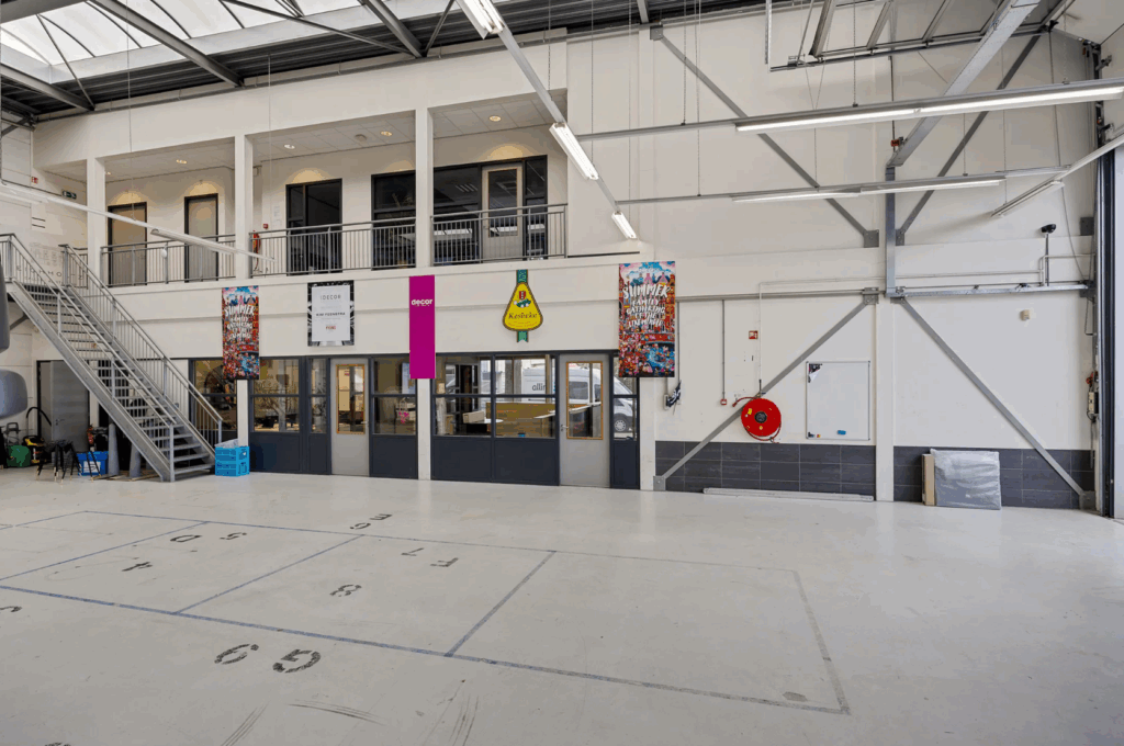 Industrial-style interior space with high ceilings, large windows, and multiple office doors and banners on the ground floor.