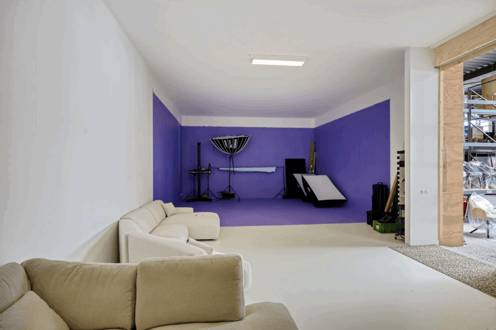 Modern photo studio with a purple backdrop, professional lighting equipment, and a beige lounge area.
