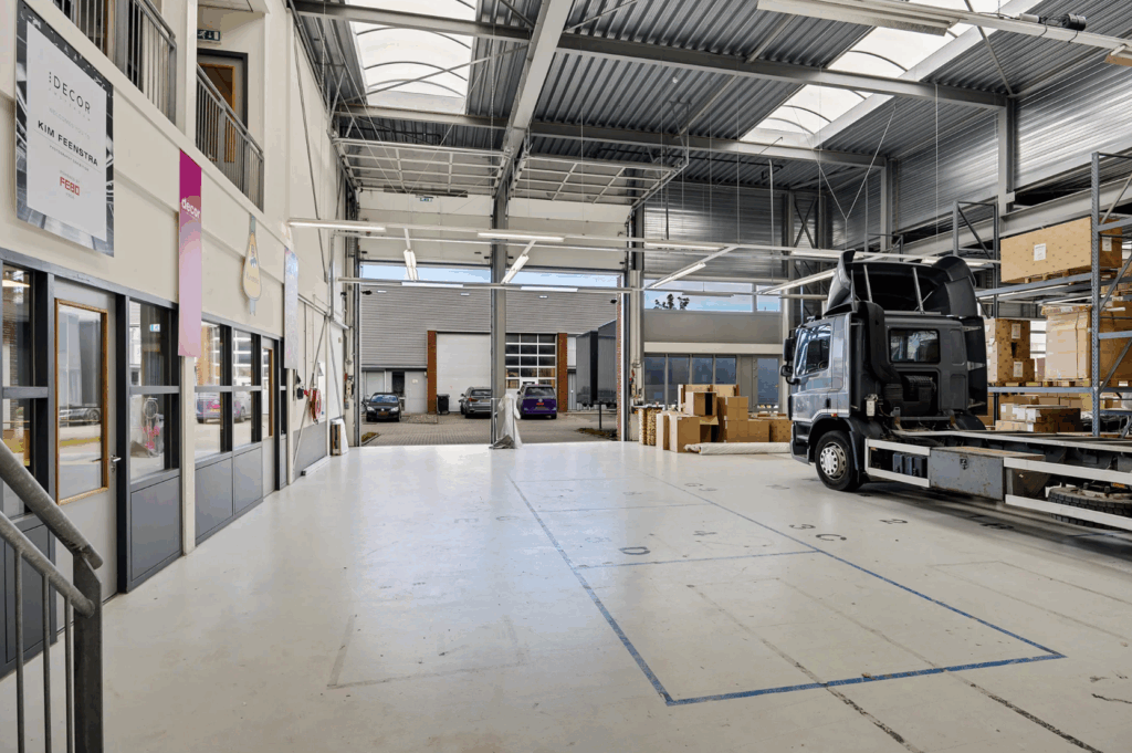 Spacious industrial warehouse with a loading truck, shelving units, and office spaces inside.