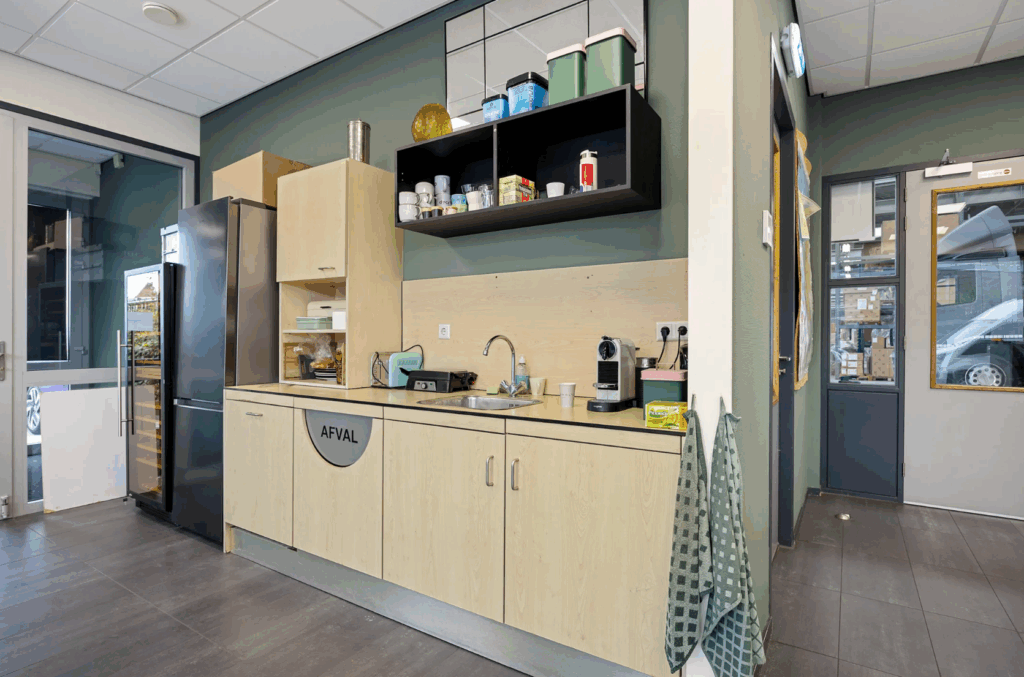 Modern office kitchenette with sink, coffee machine, fridge, and storage cabinets.