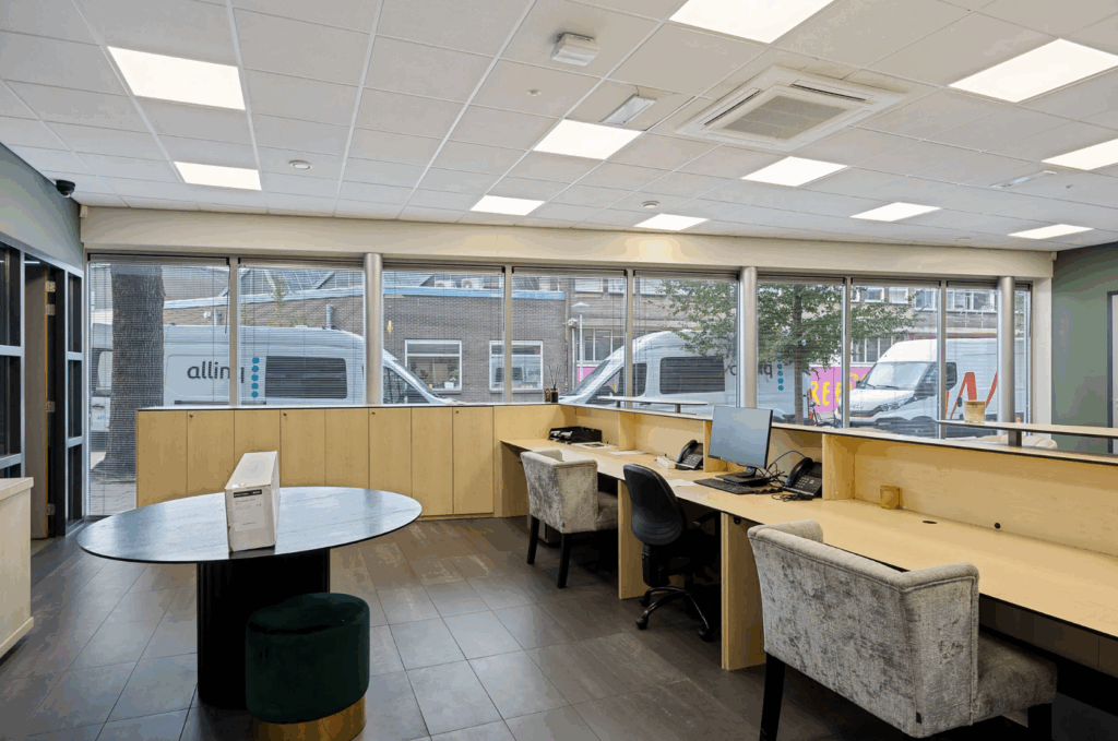 Modern office reception area with large windows, wooden desks, and multiple workstations.
