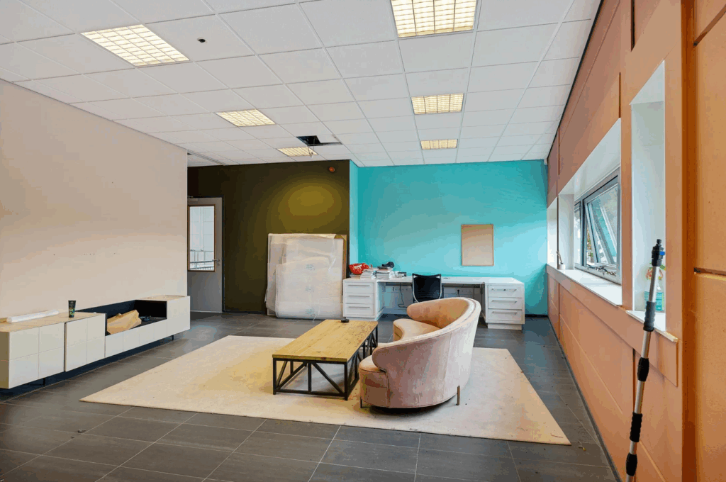 Modern office space with a pink sofa, wooden coffee table, and desks against a turquoise accent wall.