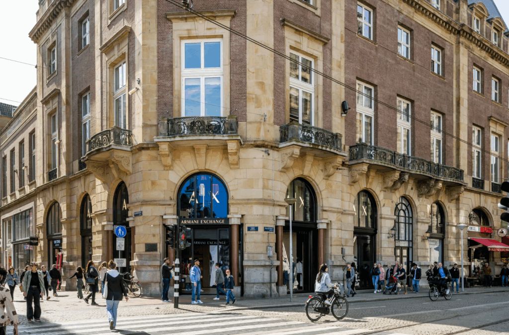 Straatbeeld van de Armani Exchange-winkel aan de Paleisstraat in een historisch gebouw met voorbijgangers en fietsers.