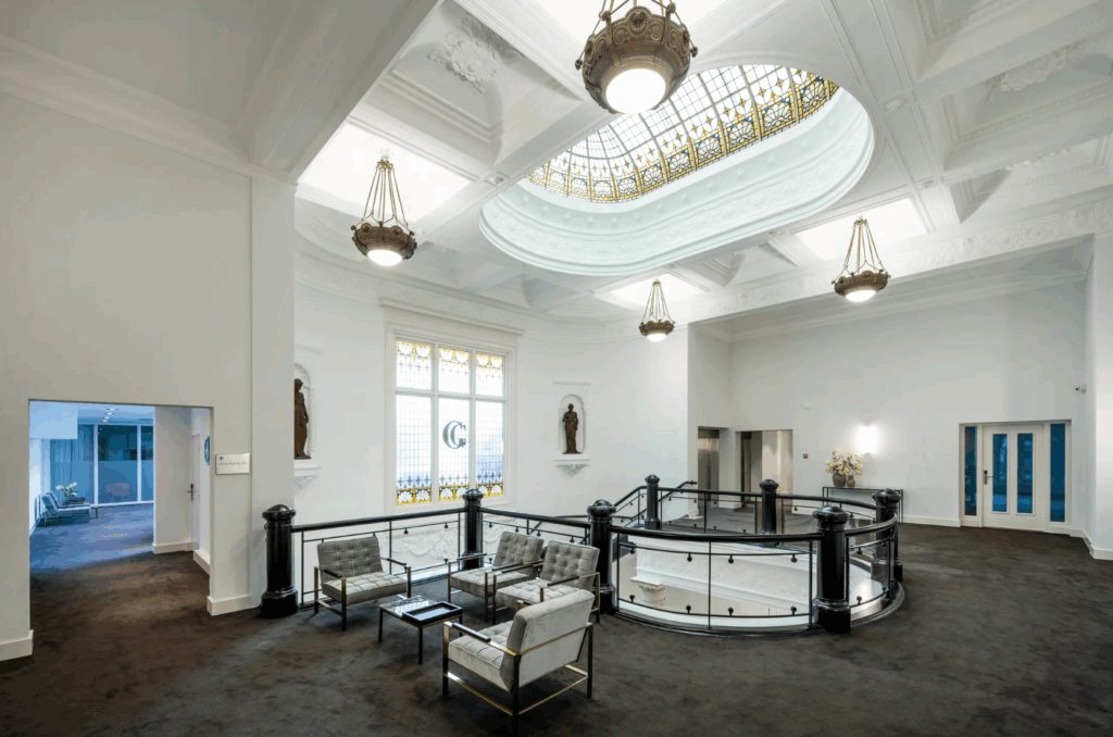 Elegante lobby in de Paleisstraat met glas-in-loodramen, sierlijk plafond en moderne loungestoelen.