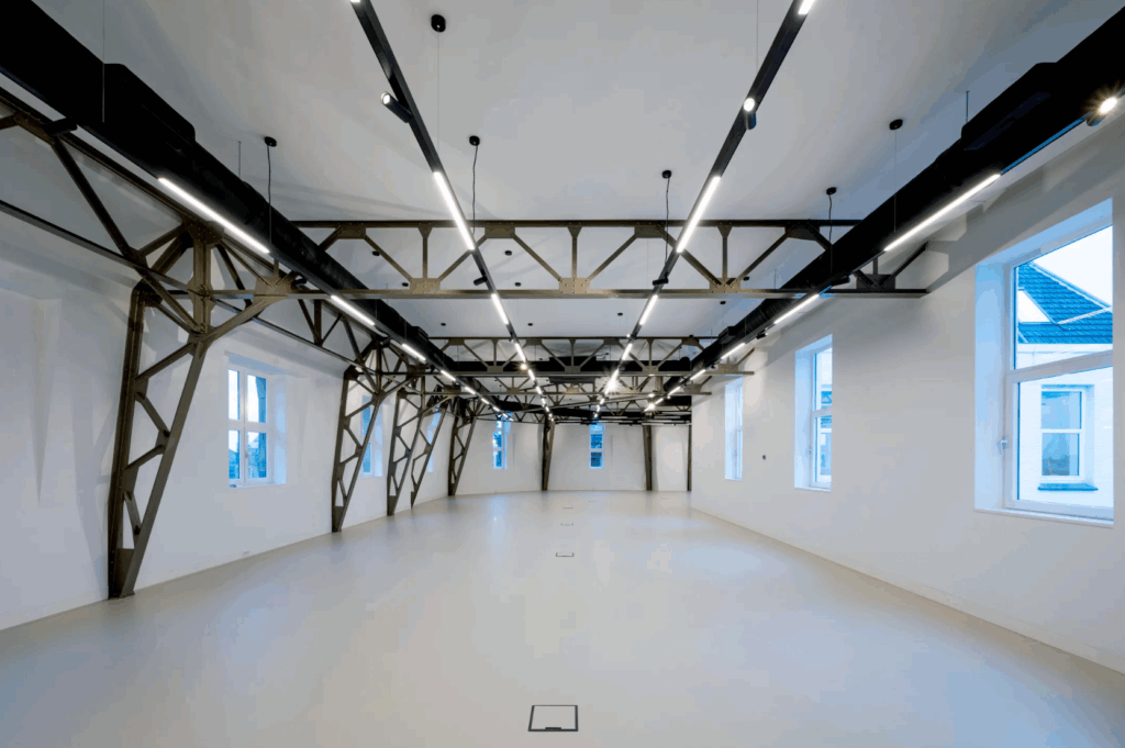 Ruim, modern interieur met zichtbare stalen balken, witte muren en grote ramen in een gerenoveerd pand aan de Paleisstraat.