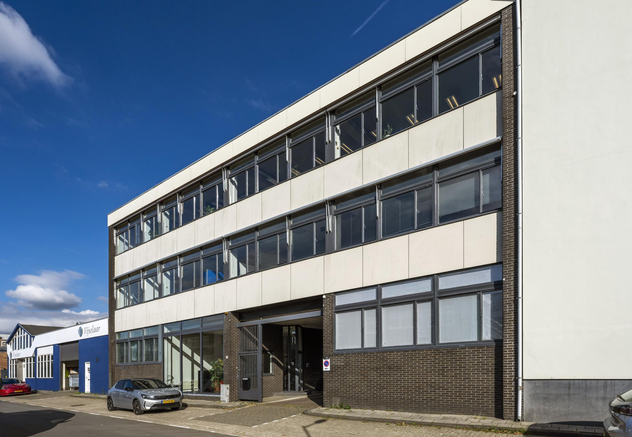 Voorgevel van een modern kantoorgebouw aan de Helicopterstraat met geparkeerde auto's ervoor.