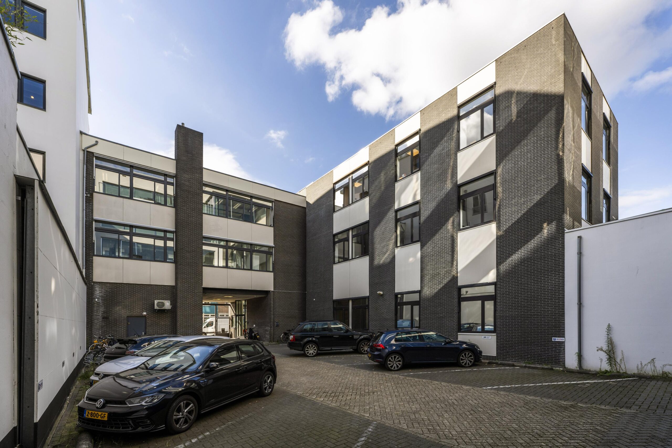 Binnenplaats met geparkeerde auto’s voor een modern kantoorgebouw aan de Helicopterstraat.