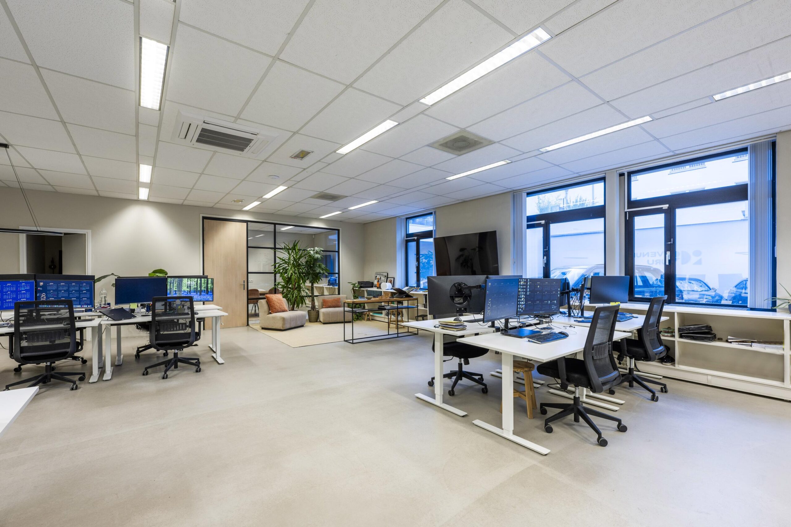 Modern en licht kantoorinterieur aan de Helicopterstraat met meerdere bureaus, computerschermen en een loungehoek.