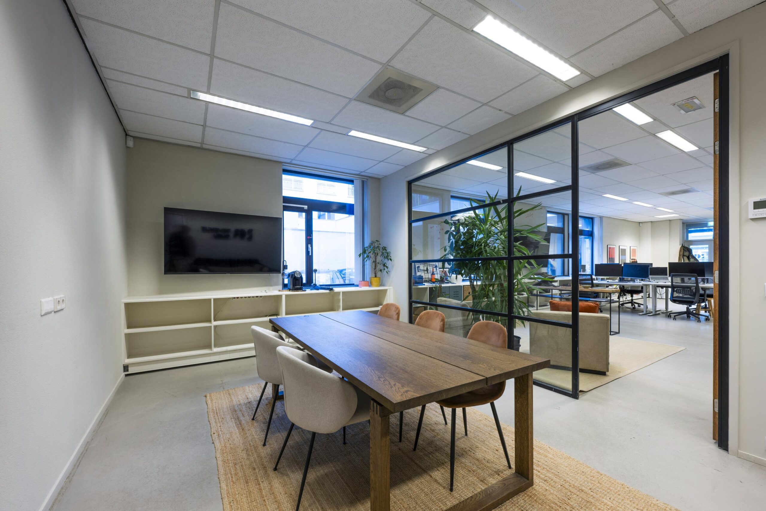 Vergaderruimte met houten tafel en zes stoelen, grenzend aan een open kantoortuin aan de Helicopterstraat.