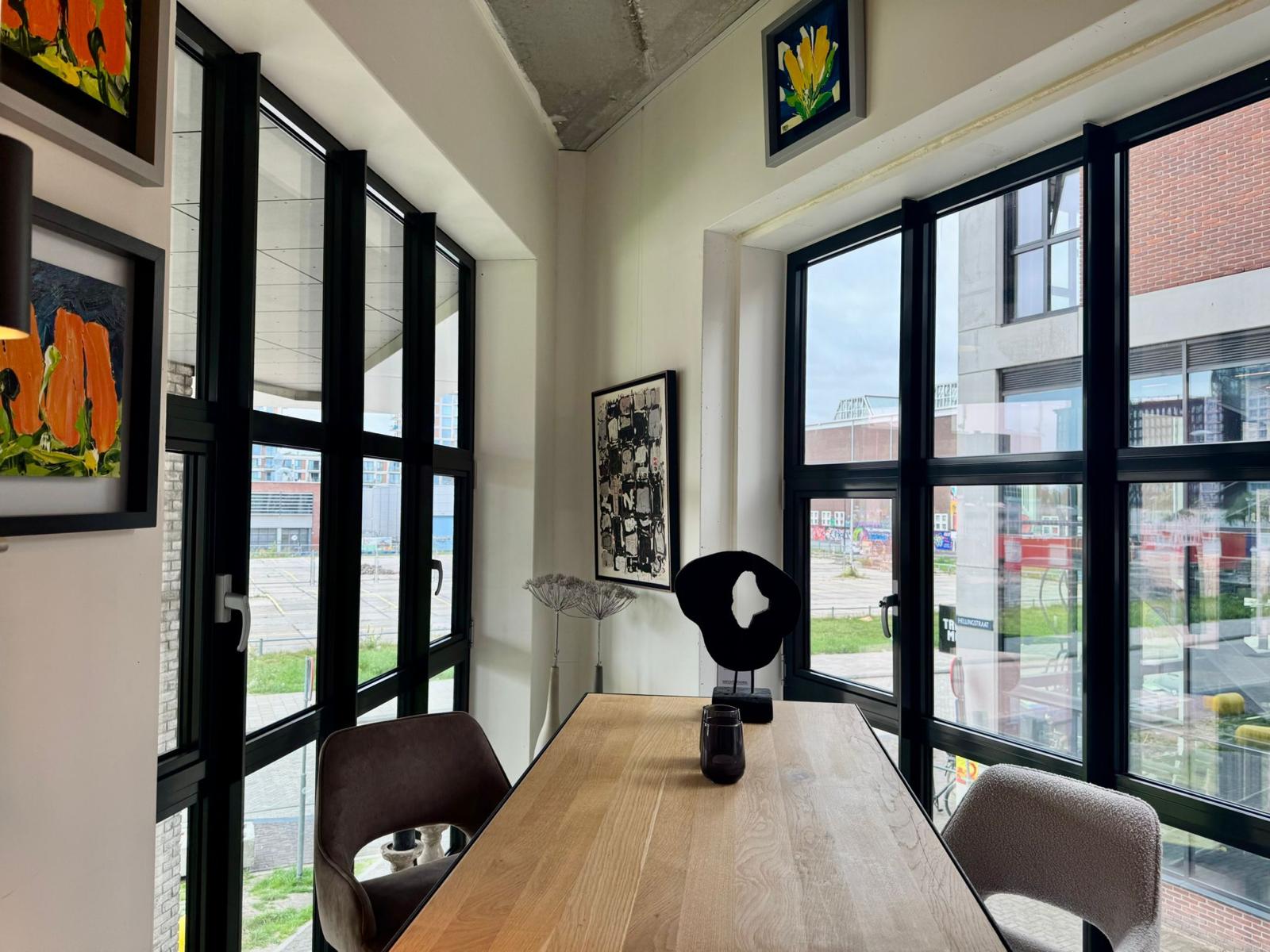 Kleine eethoek met moderne kunst aan de muur en uitzicht op een stedelijke omgeving door grote ramen.