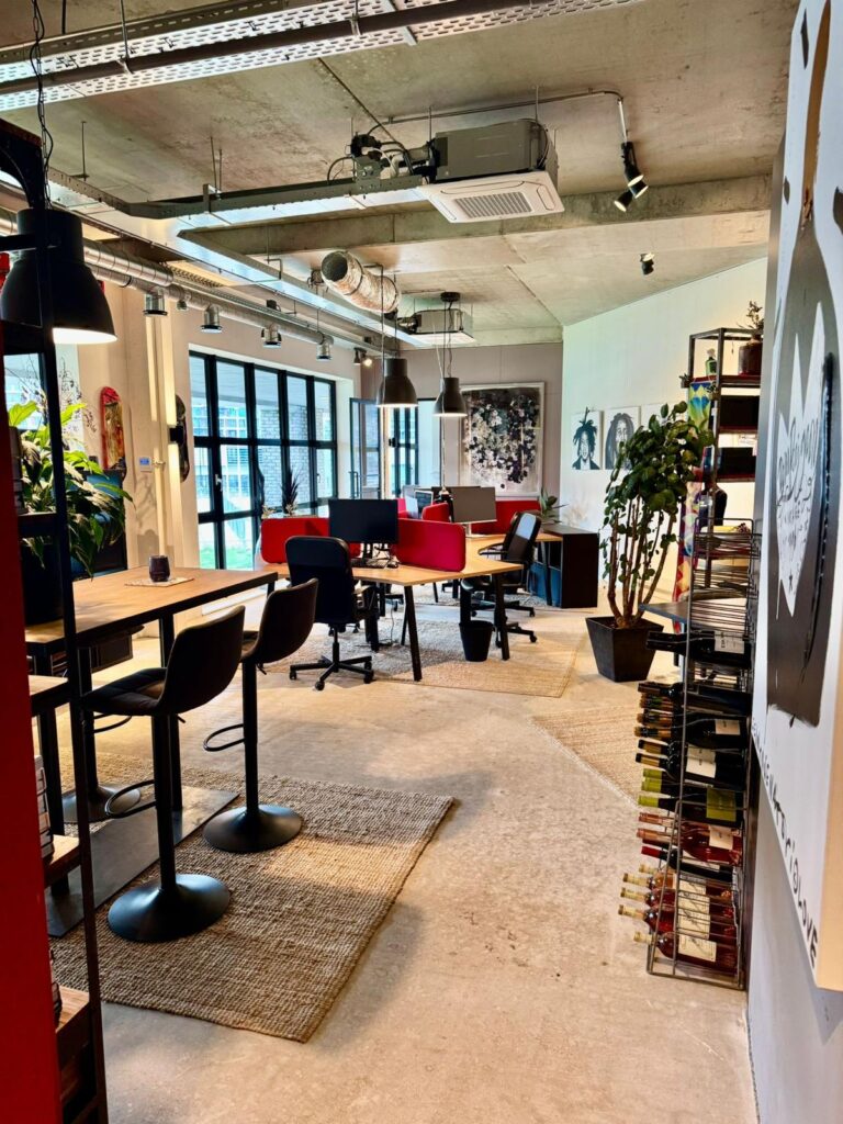 Modern industrial-style office space with wooden desks, black and red chairs, and exposed ceiling ducts.