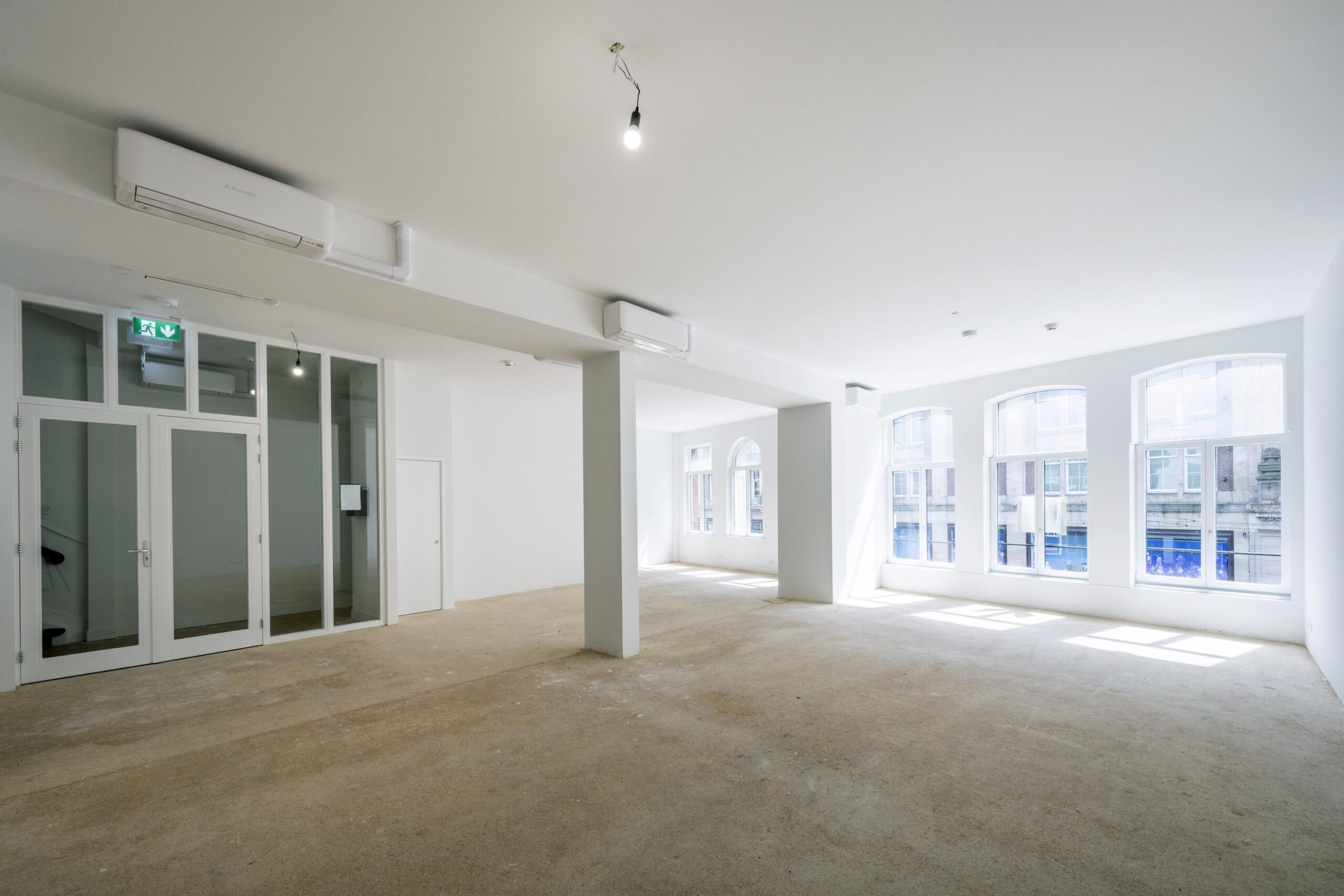 Lichte, lege kantoorruimte aan de Damrak met grote ramen en witte muren.