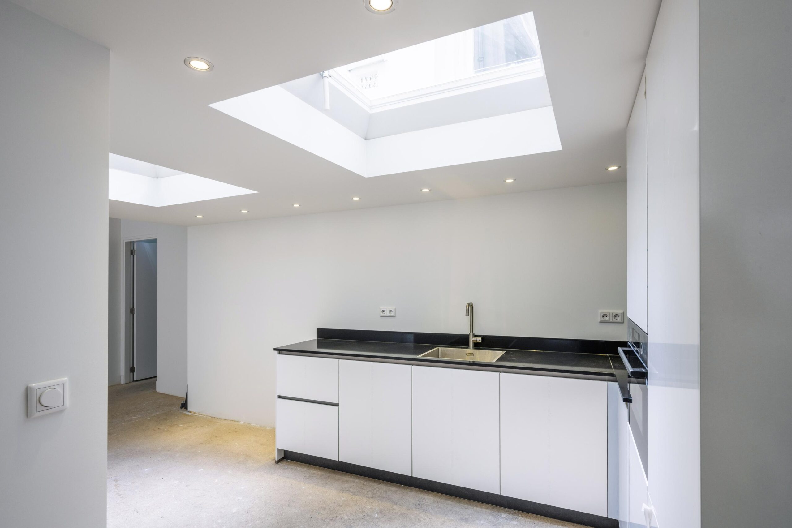 Moderne witte keuken met zwart aanrechtblad en lichtinval via twee grote dakramen.