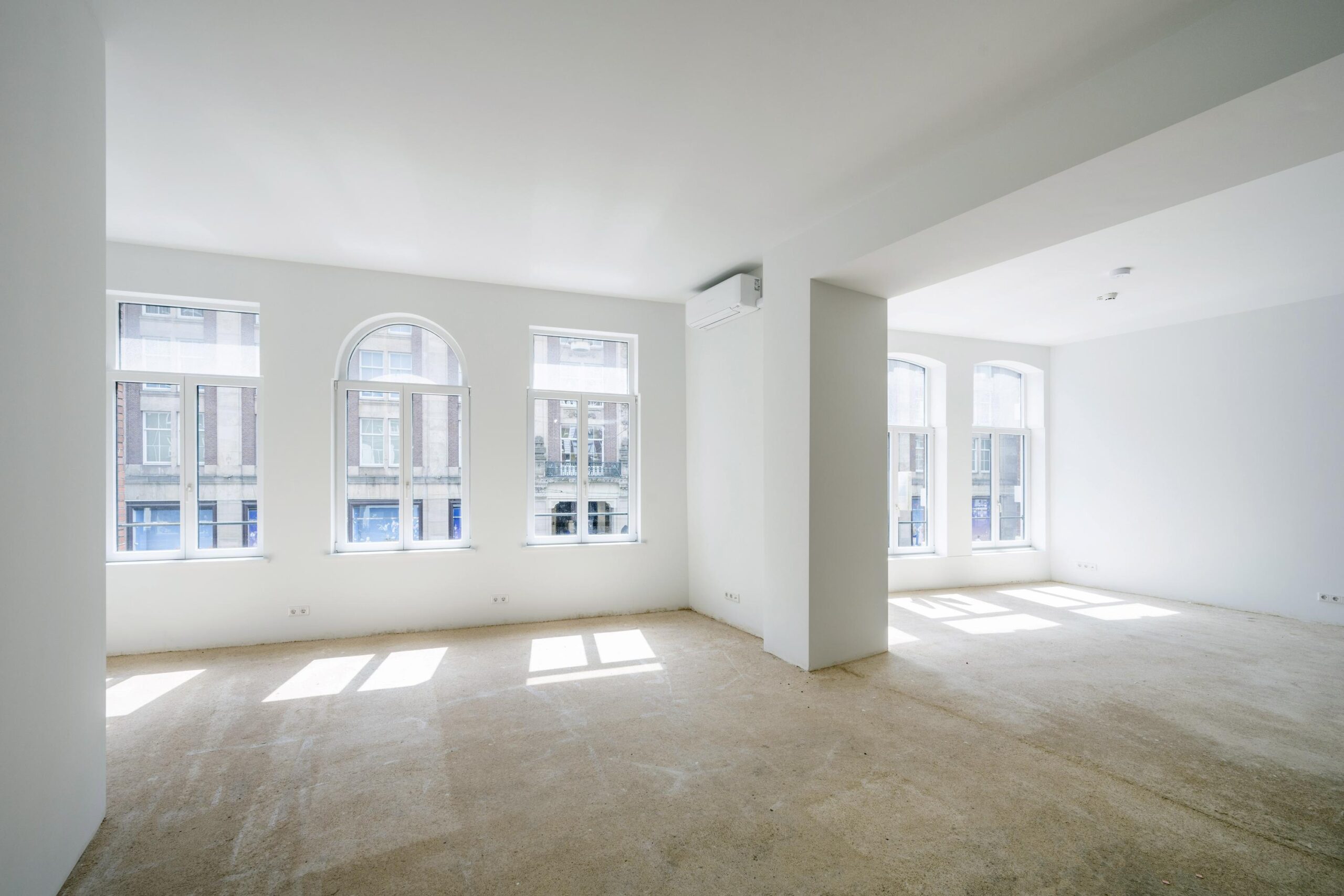 Lichte, lege ruimte met grote ramen en uitzicht op de gebouwen aan de Damrak in Amsterdam.