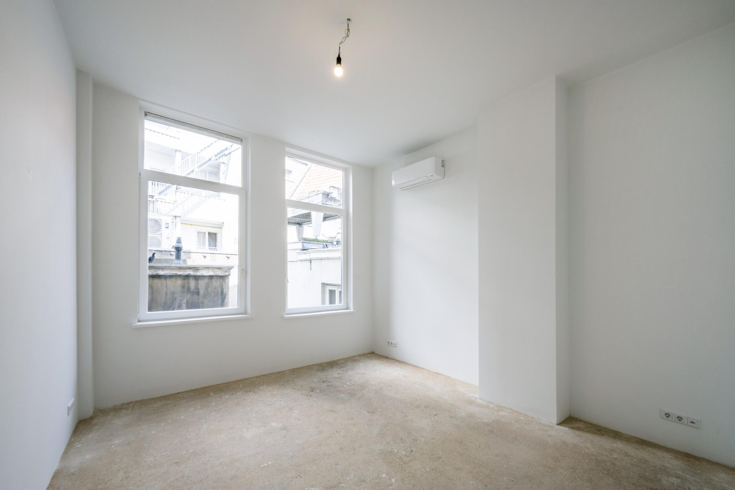 Leeg, witgeschilderd vertrek aan het Damrak met twee ramen, airco en onafgewerkte vloer.