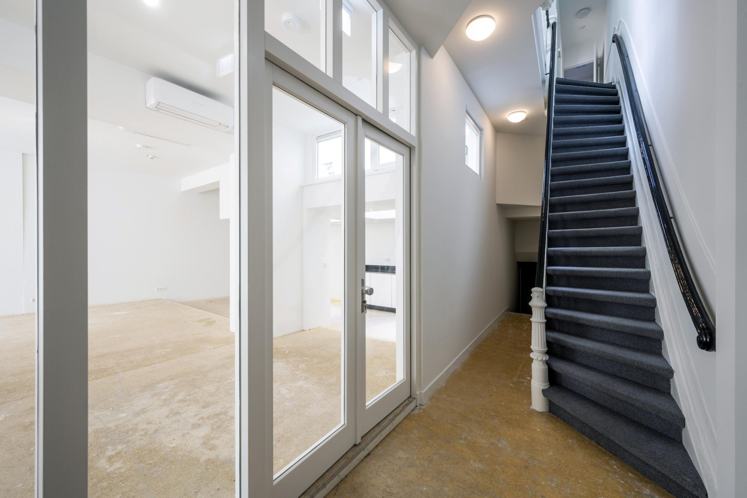 Inpandige hal met trap en doorkijk naar een lege ruimte op de begane grond van een pand aan het Damrak.