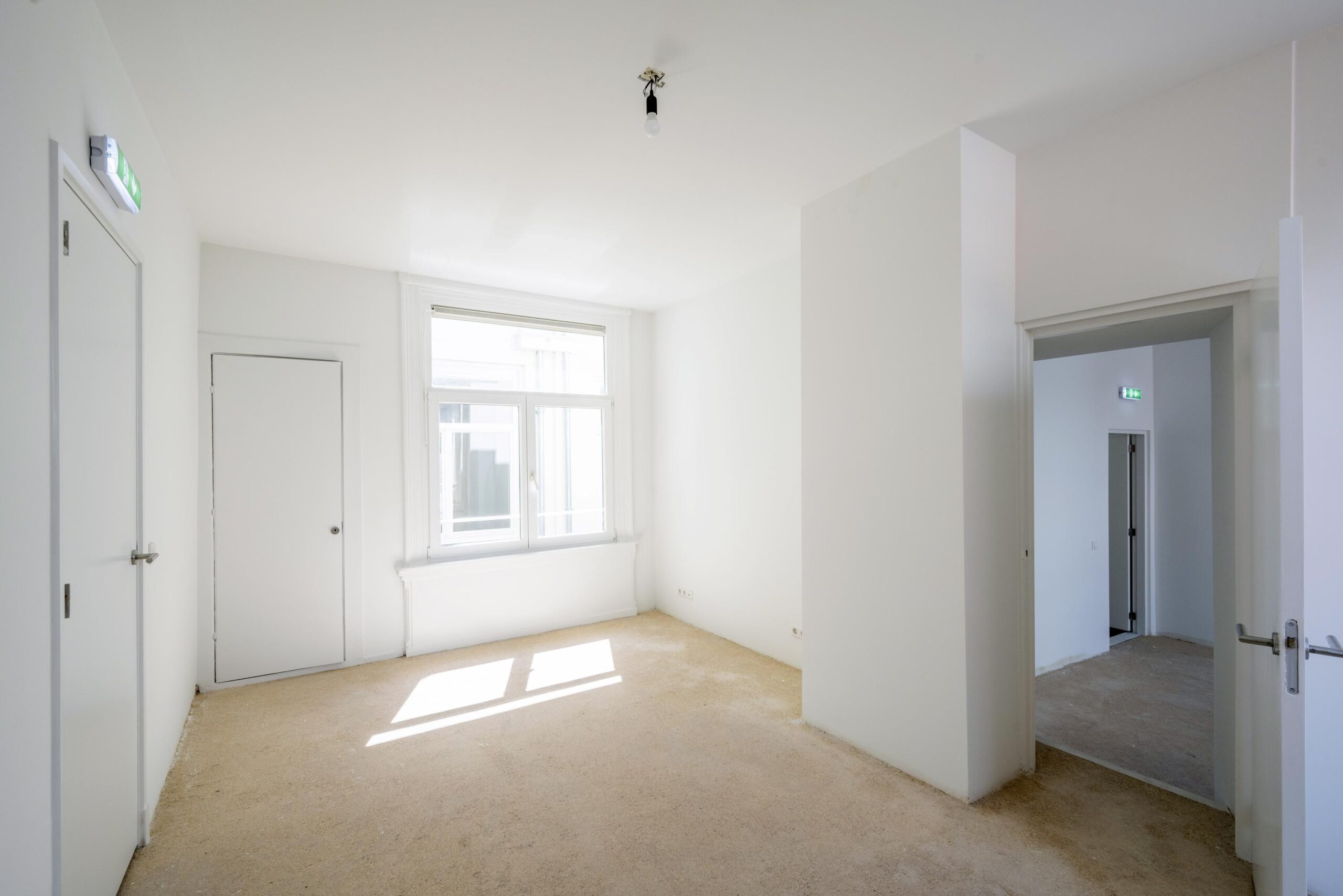 Leeg, witgeschilderd vertrek met groot raam en open doorgang aan de Damrak.