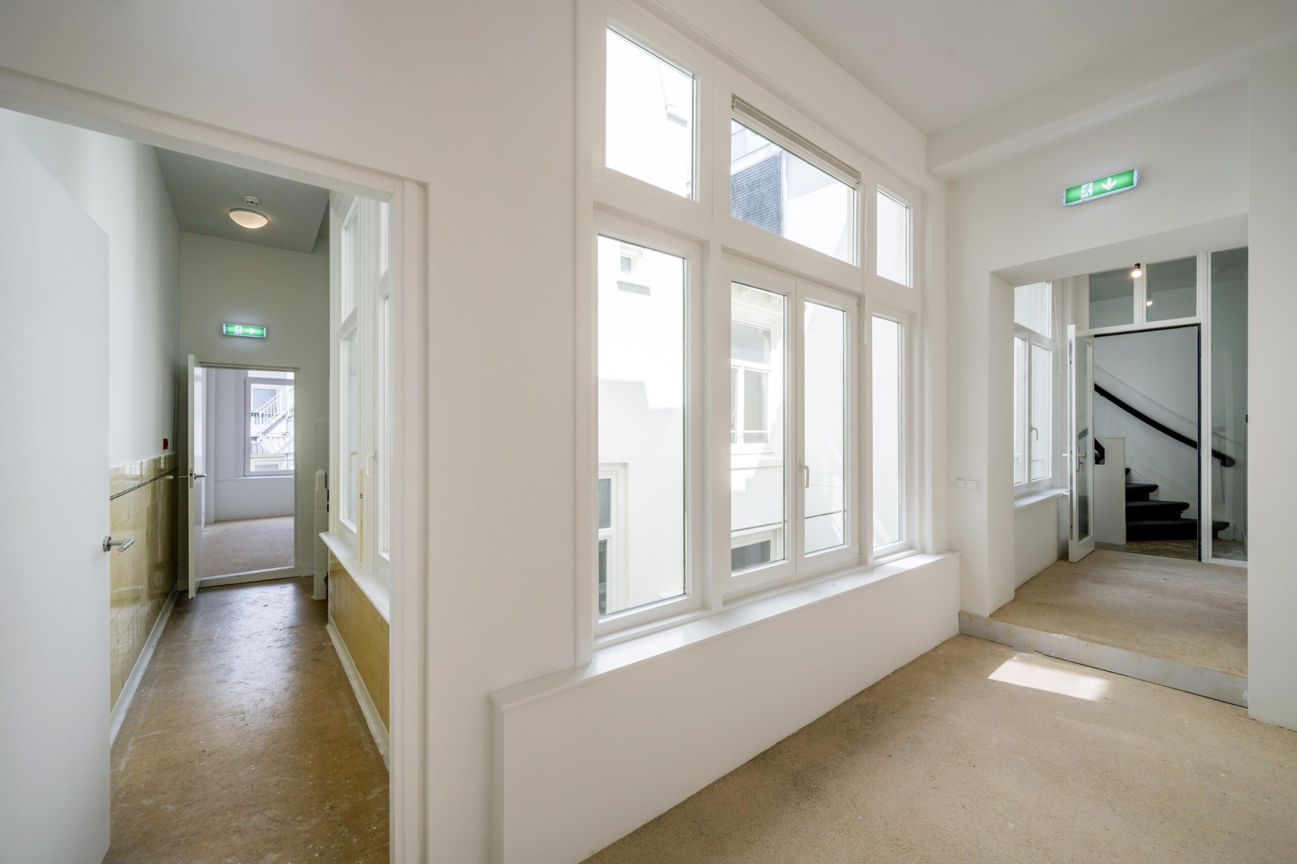 Licht trappenhuis met grote ramen en gang in een pand aan het Damrak.