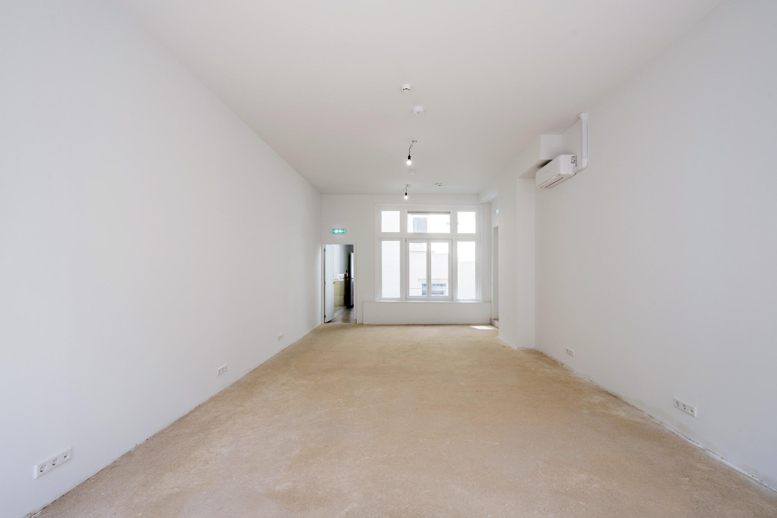 Leegstaand, licht appartement aan het Damrak met witte muren, grote ramen en onafgewerkte vloer.