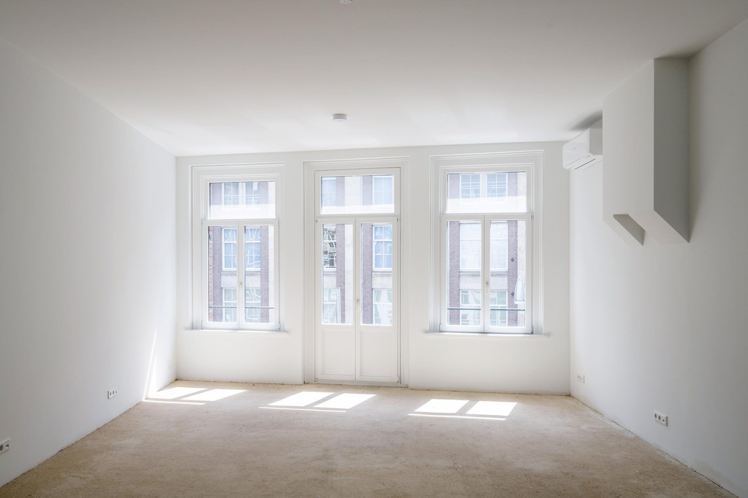 Licht en leeg appartement aan het Damrak met grote ramen en witte muren.