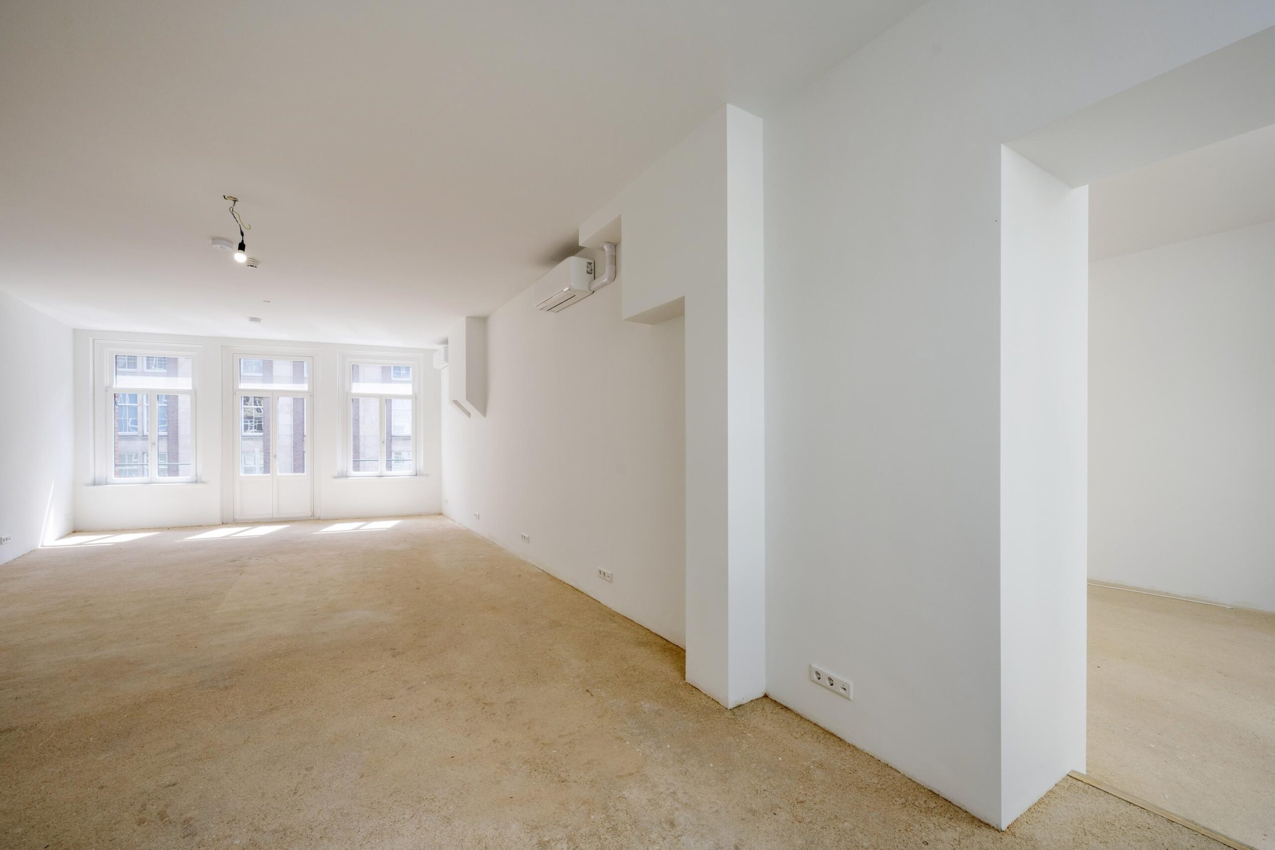 Lichte, lege woonruimte op de Damrak met grote ramen en witte muren.