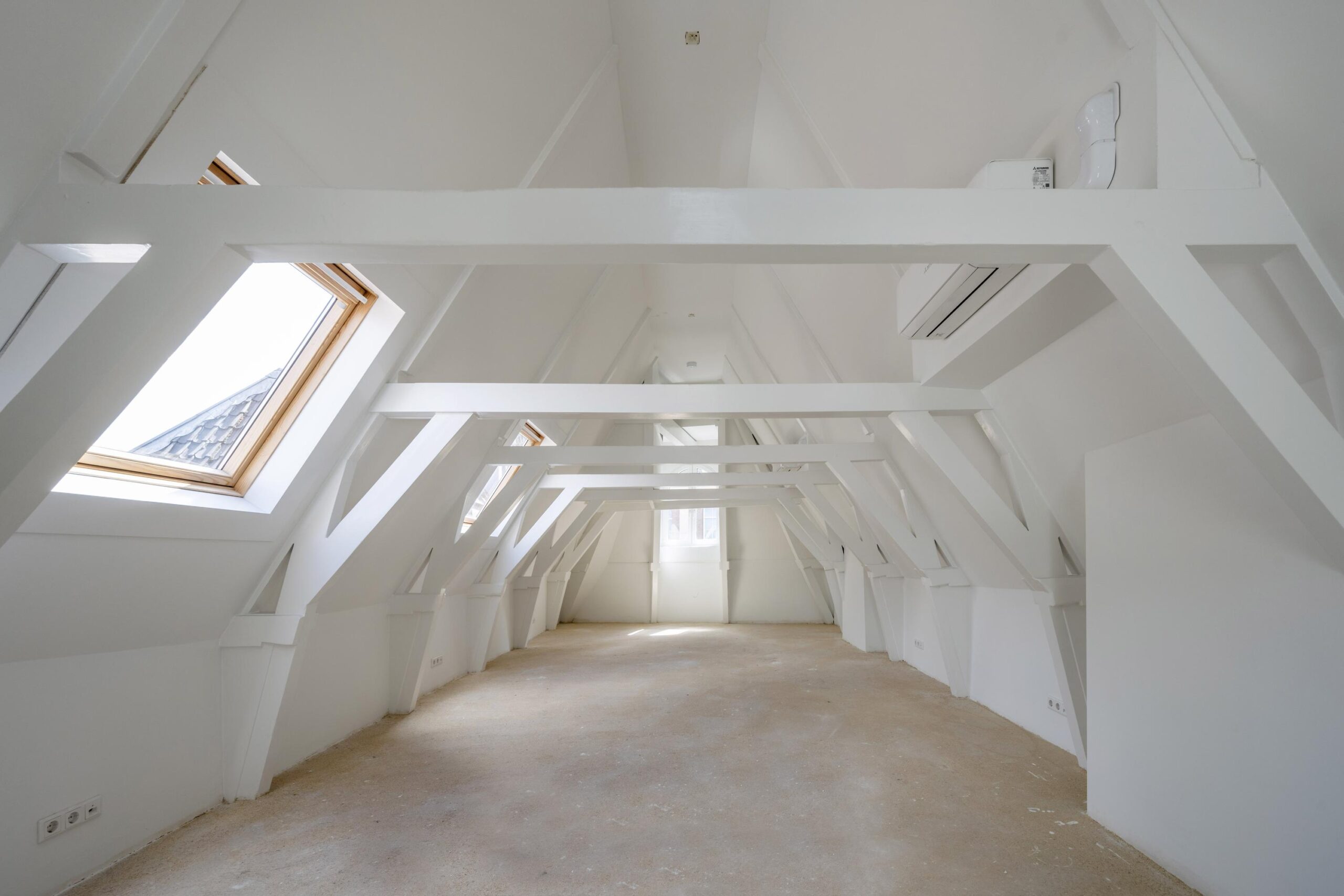Lichte, open zolderruimte aan het Damrak met witte balkenconstructie, schuine dakramen en airconditioning.
