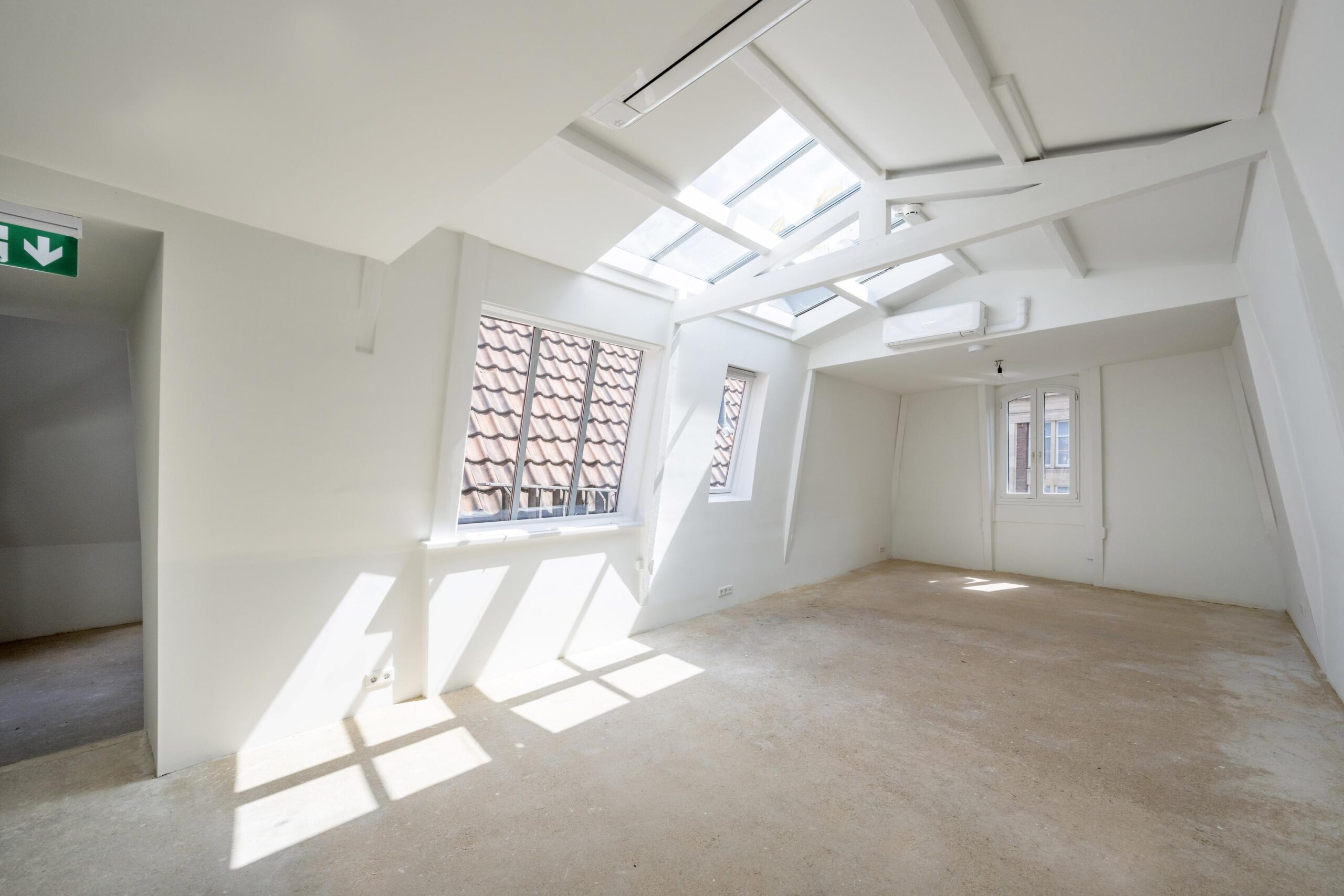 Lichte, lege zolderruimte aan het Damrak met schuin dak, dakramen en zicht op rode dakpannen.