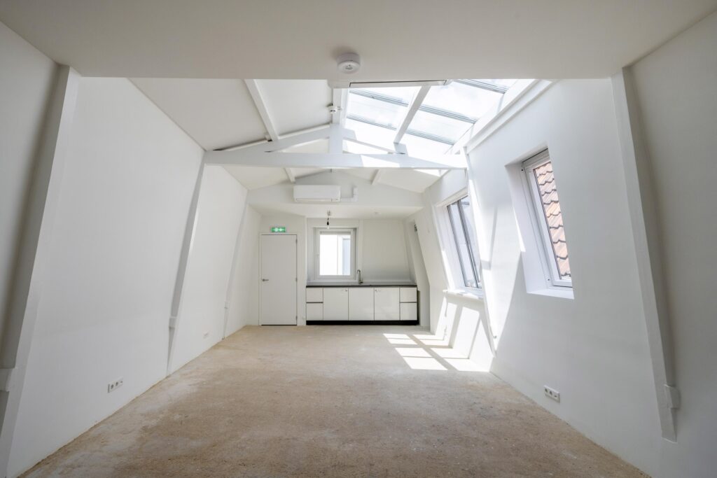 Lichte, lege zolderruimte aan het Damrak met schuine witte wanden, dakramen en een kleine kitchenette.