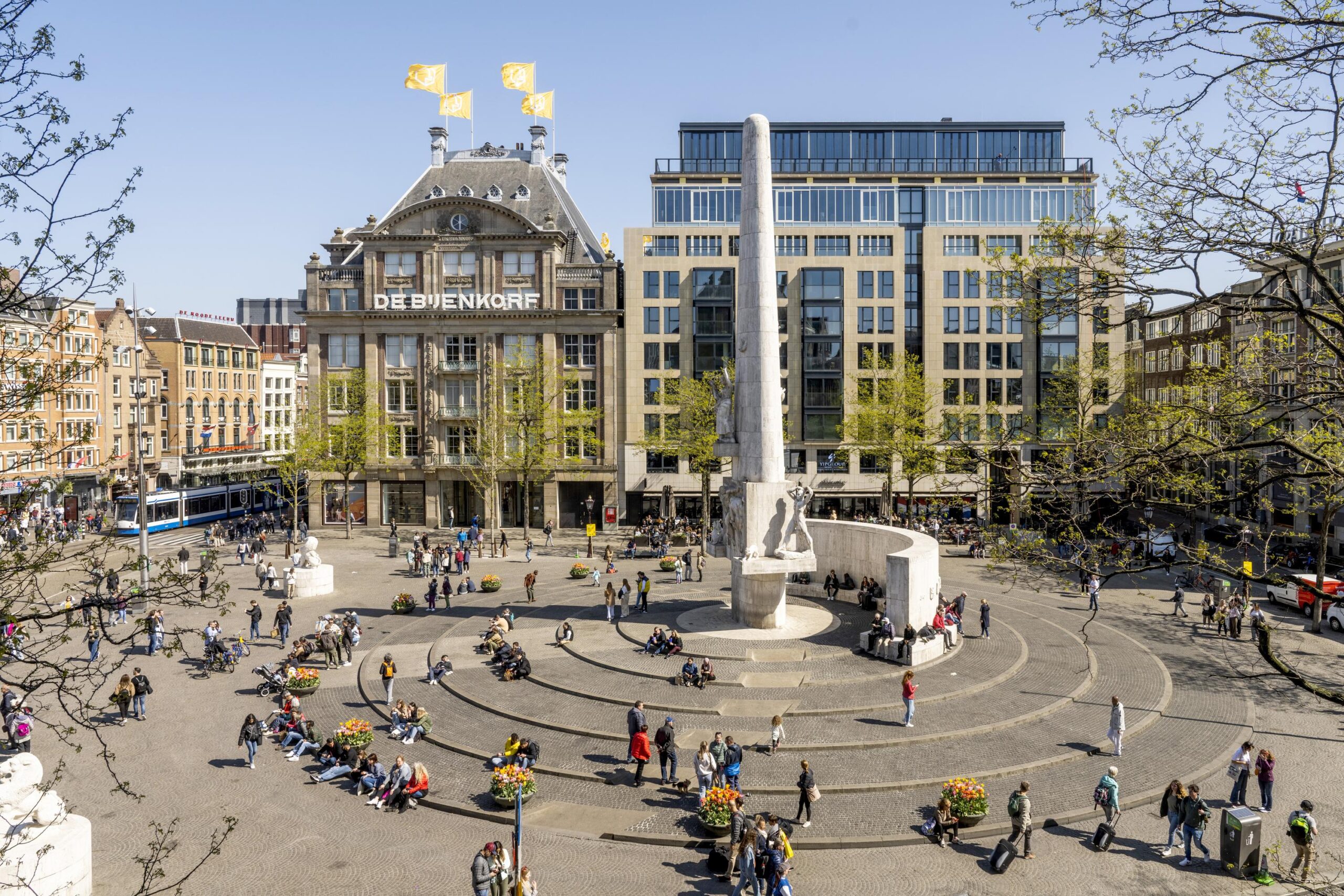 Drukbezocht Nationaal Monument op de Dam in Amsterdam met op de achtergrond warenhuis De Bijenkorf.