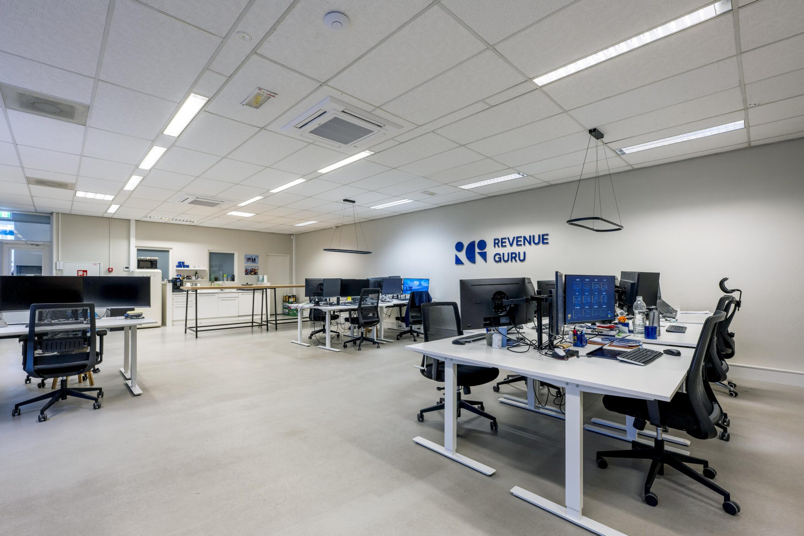 Modern kantoorinterieur van Revenue Guru aan de Helicopterstraat met werkplekken, computers en een open keukengedeelte.