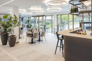 Modern, stylish office lounge with a bar, seating area, and large windows overlooking a garden.