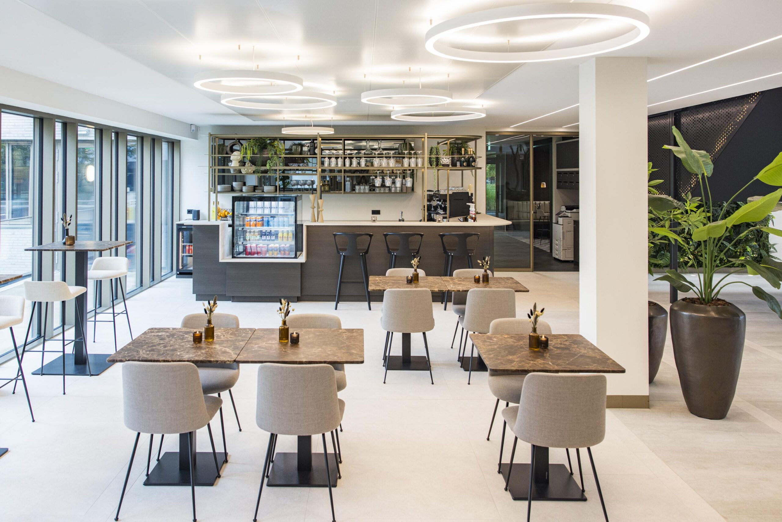 Modern office café with stylish seating, a central bar, and large windows providing natural light.
