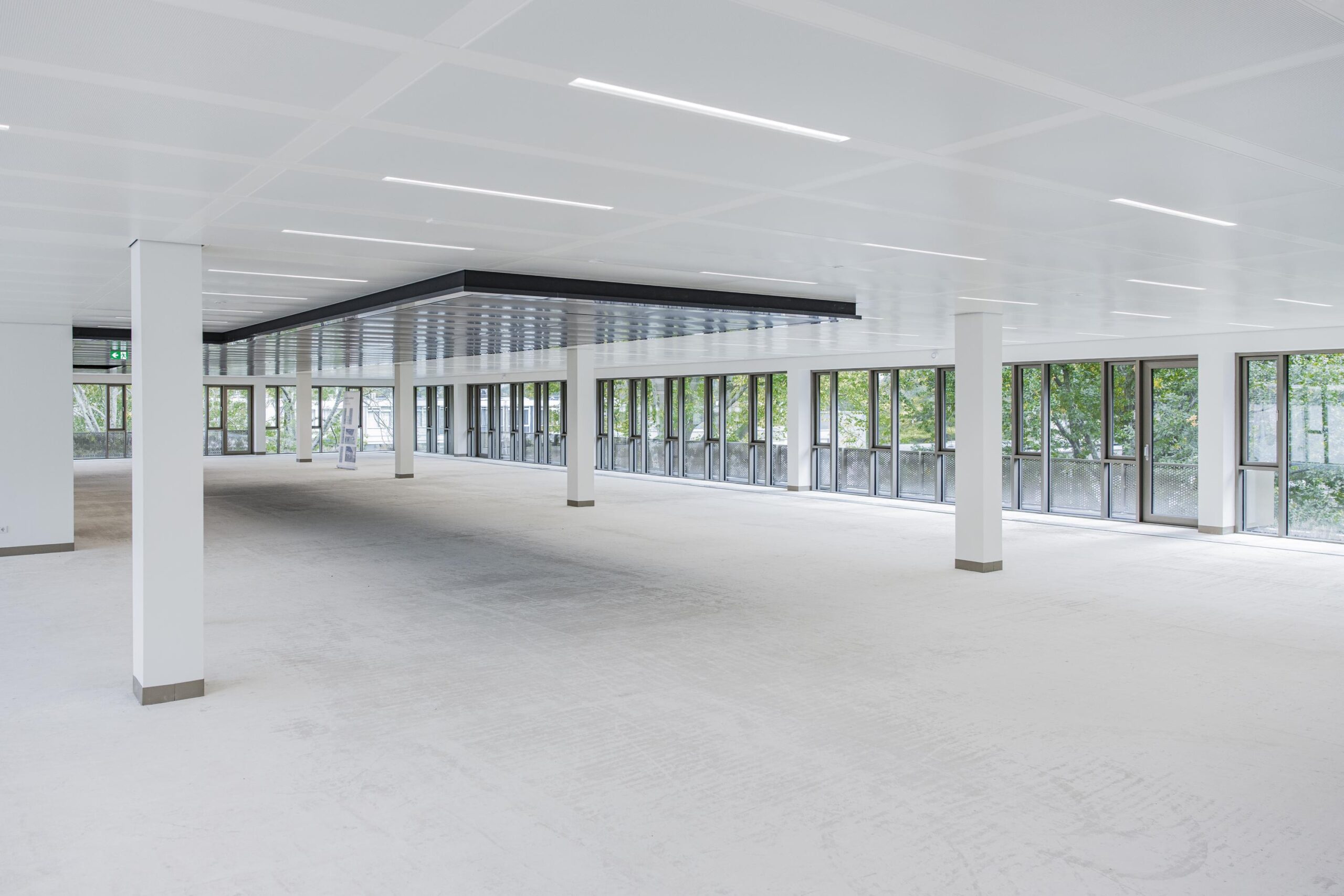 Spacious, empty office floor with large windows and modern white ceiling panels.