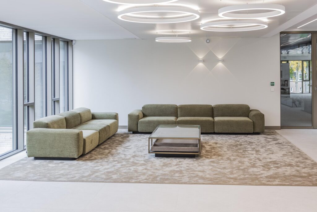 Modern lounge area with green sofas, a glass coffee table, and circular ceiling lights in the Walborg building.