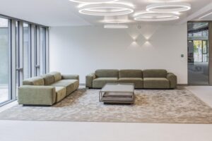 Modern lounge area with green sofas, a glass coffee table, and circular ceiling lights in the Walborg building.