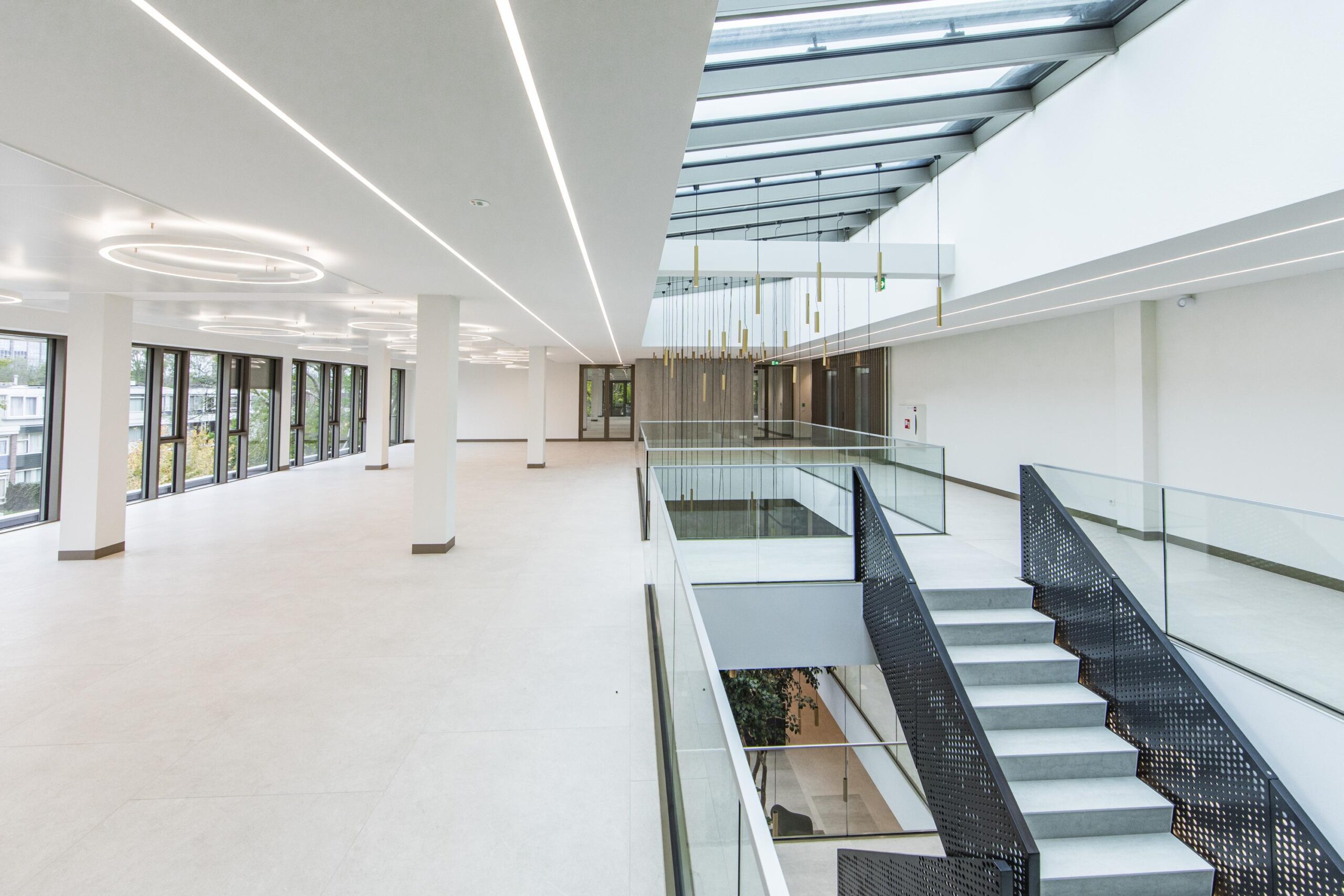 Modern, spacious office interior with large windows, minimalist lighting, and a central staircase.
