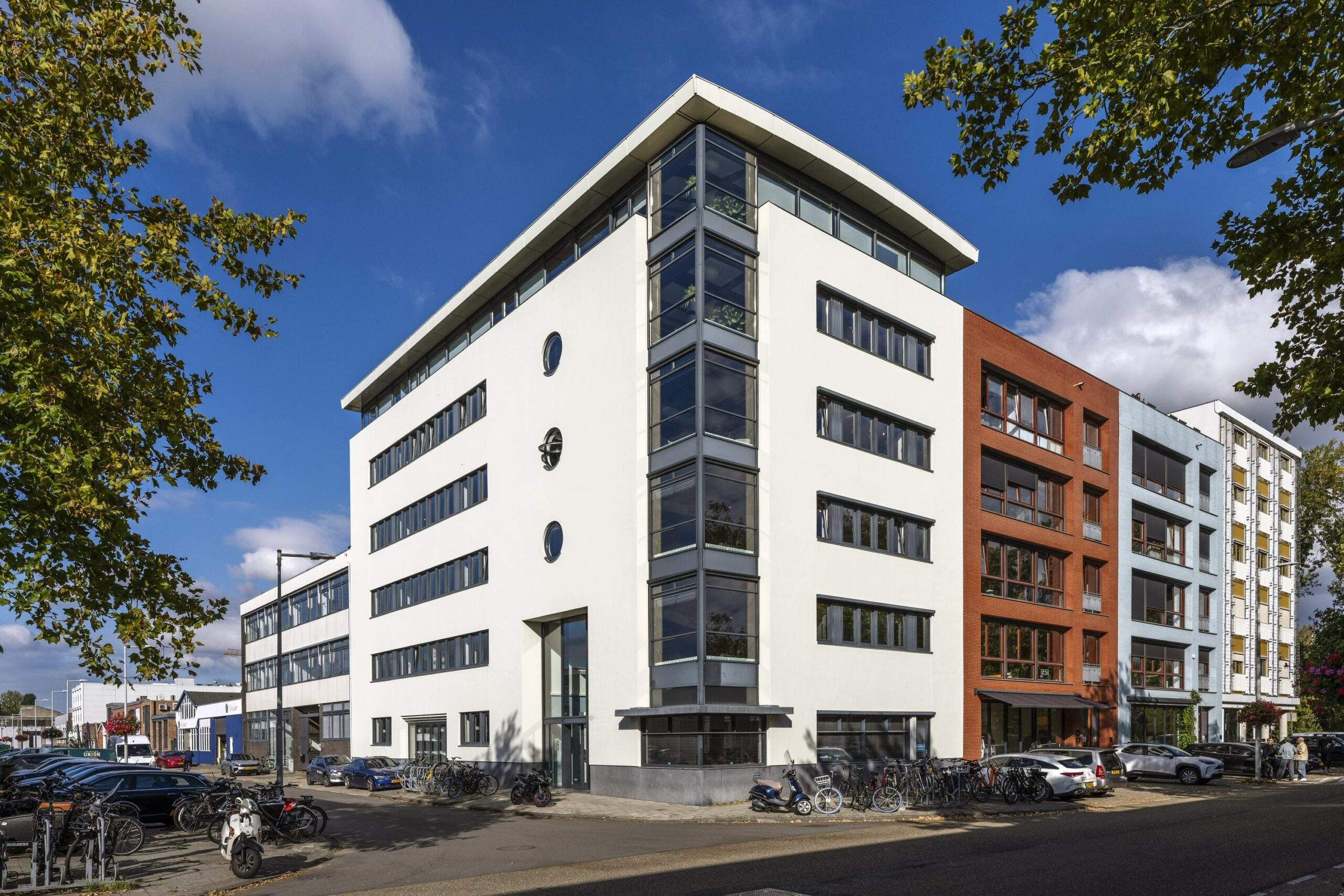 Modern apartment and office buildings on Helicopterstraat with parked cars and bicycles in front.