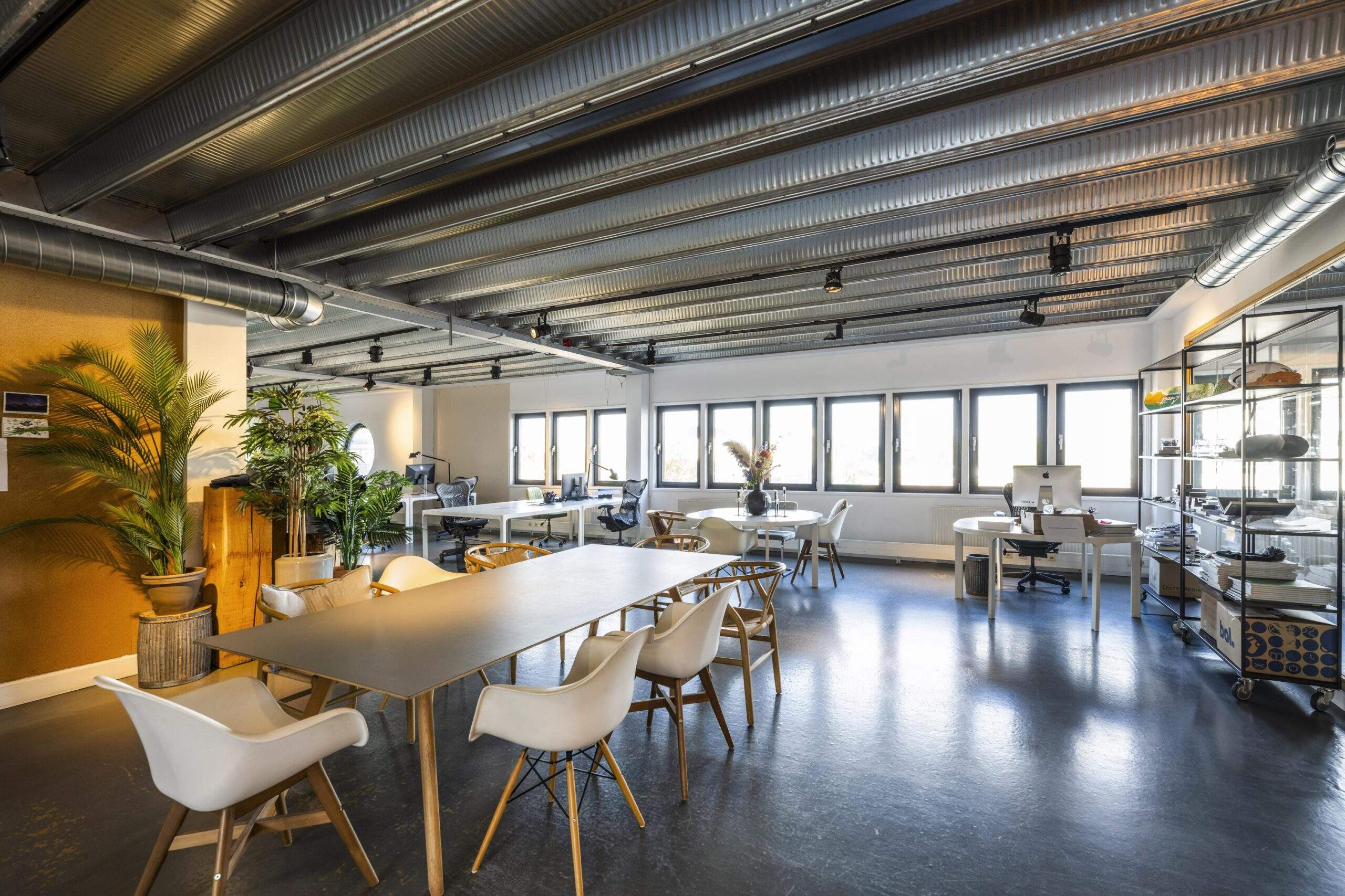Modern open-plan office space on Helicopterstraat with industrial ceiling, large windows, and stylish furniture.