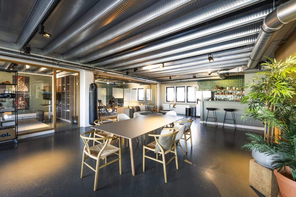 Modern office space on Helicopterstraat with a meeting table, lounge area, bar, and industrial-style ceiling.